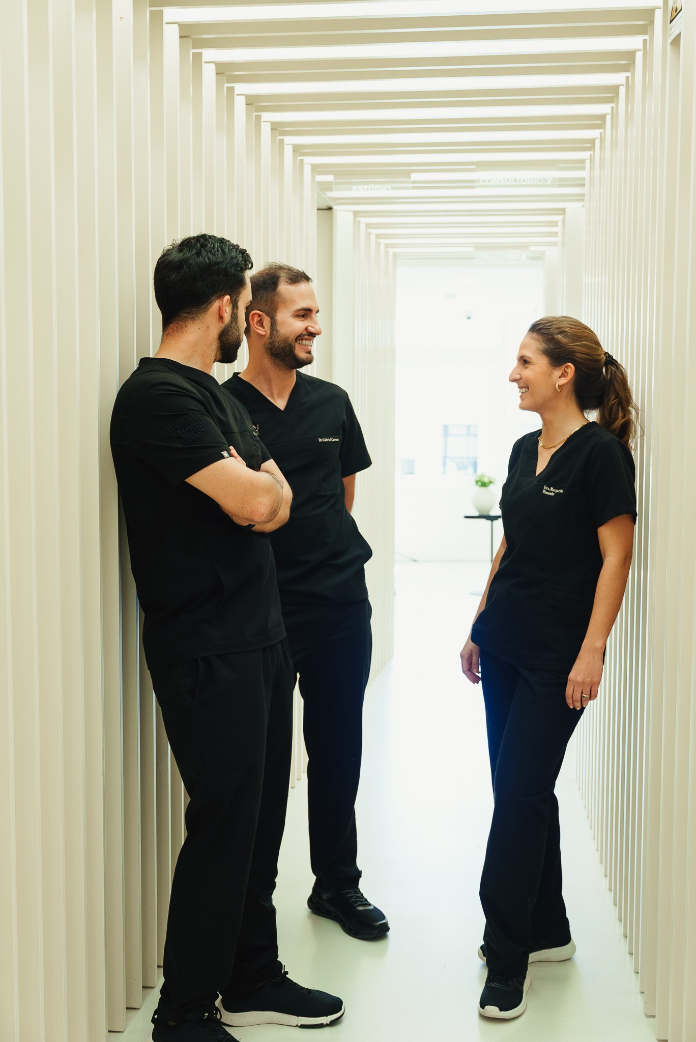 Fotografia corporativa de equipa médica com três profissionais em fardamento preto a conversar num corredor moderno de clínica, captada pela Khave Media