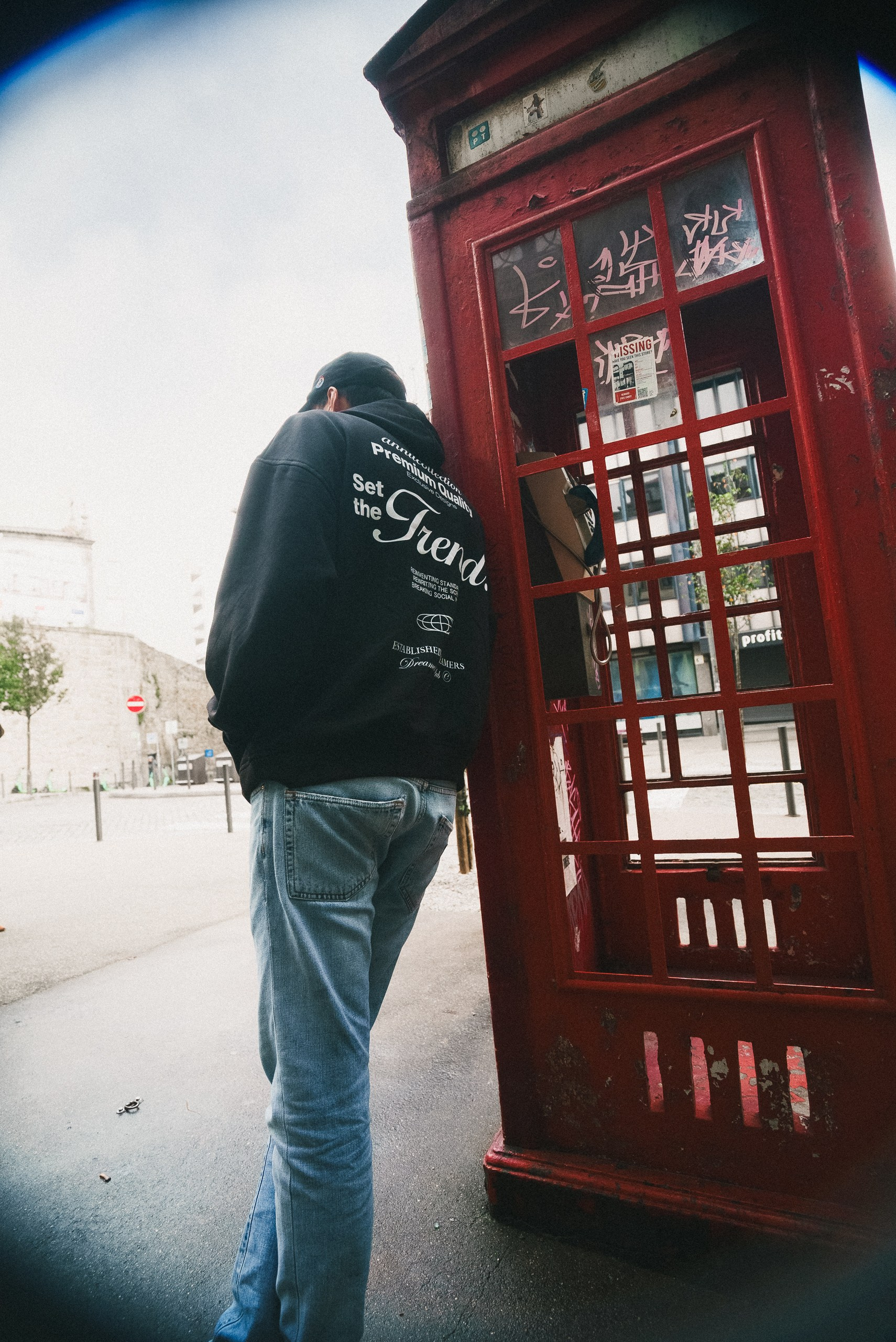 Fotografia urbana em olho de peixe de um jovem com hoodie junto a uma cabine telefónica vermelha, captada pela Khave Media