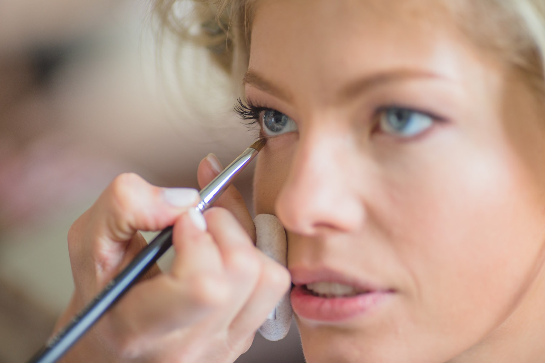 Makeup artist applying eyeliner to Swiss bride Julia during wedding morning in Prague.