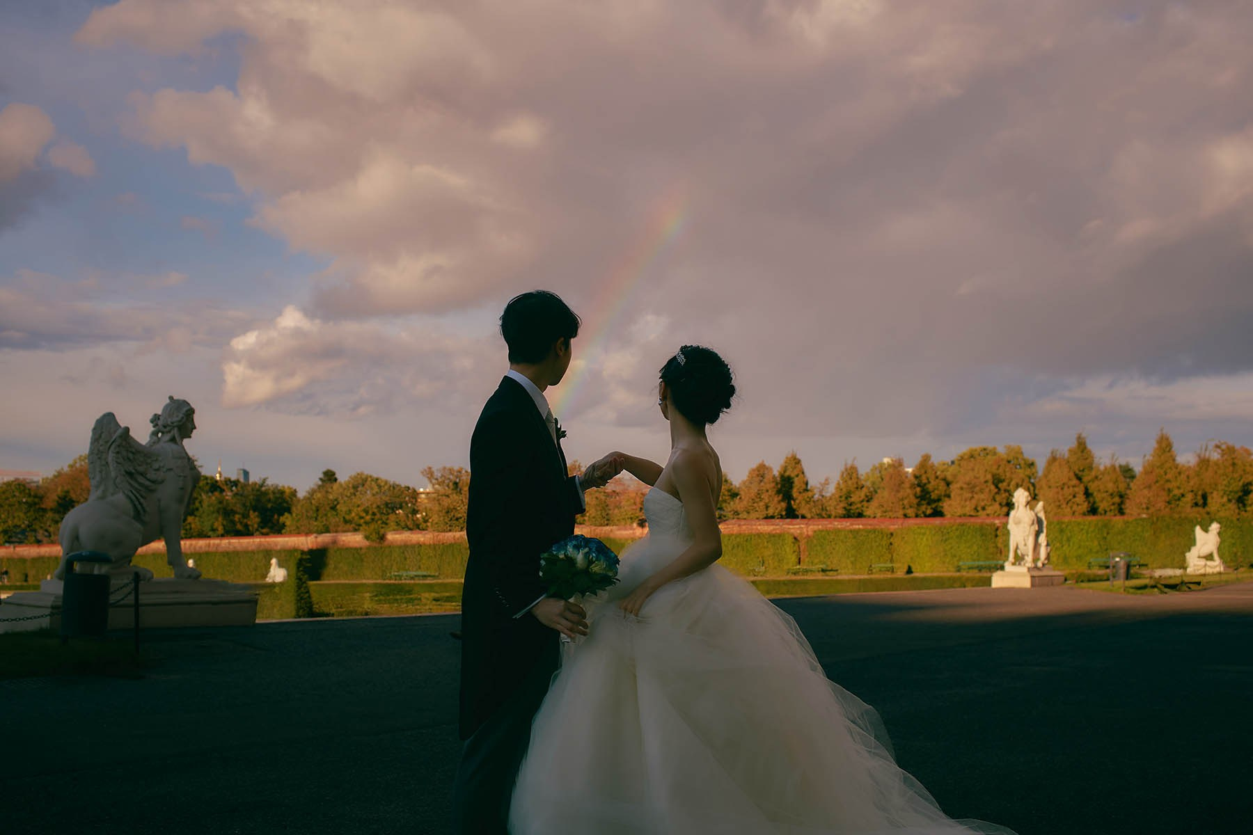 Newlyweds silhouetted with rainbow at Belvedere Palace Vienna.