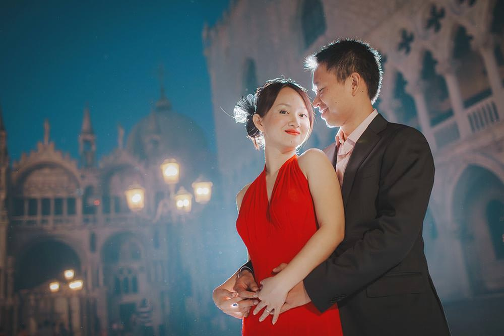 A stylish Thai couple embraces under the gas lamps in San Marco during their nighttime pre-wedding portrait session in Venice.