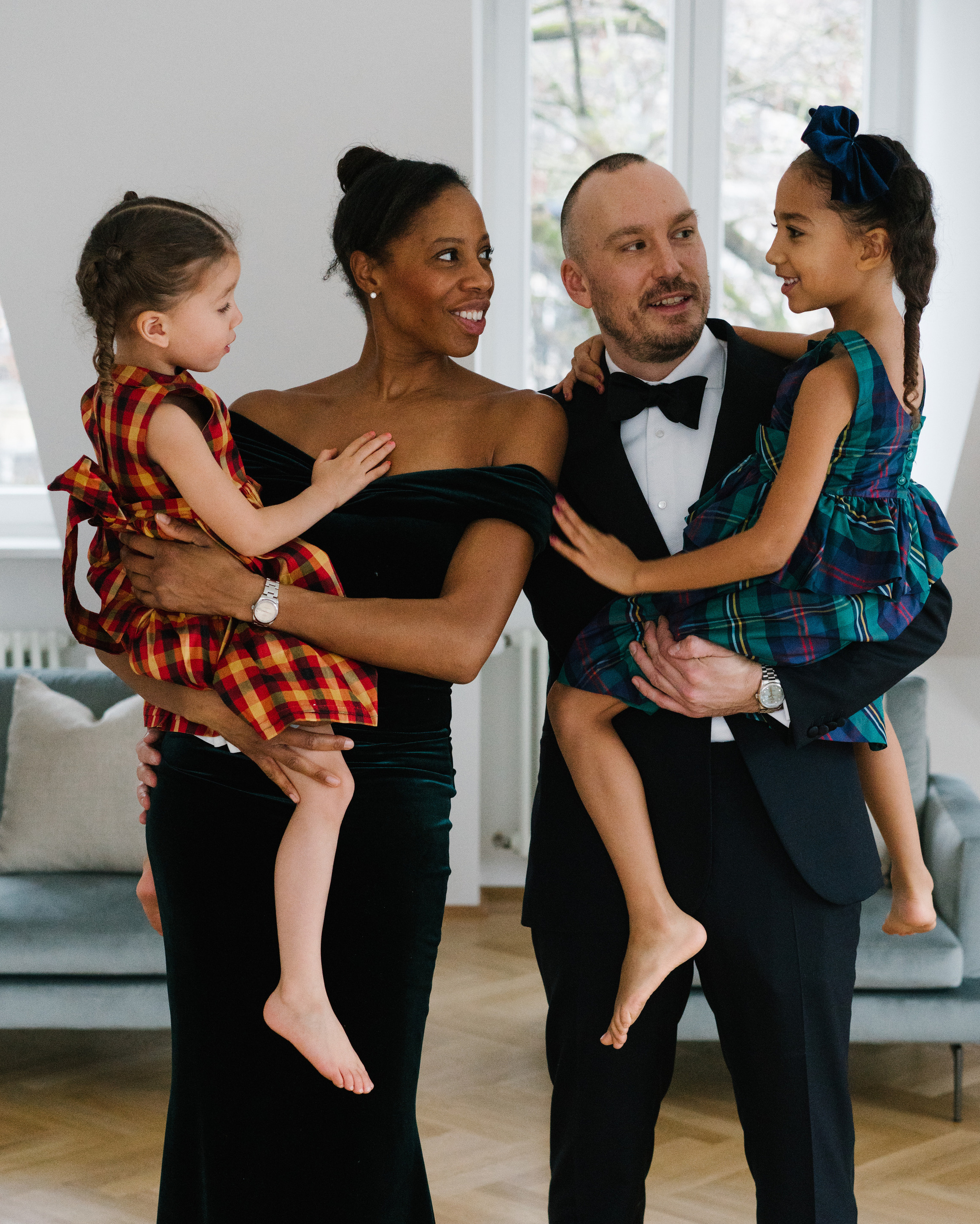 Mother and father in black tie classic outfits are holding their daughters during Christmas photo session