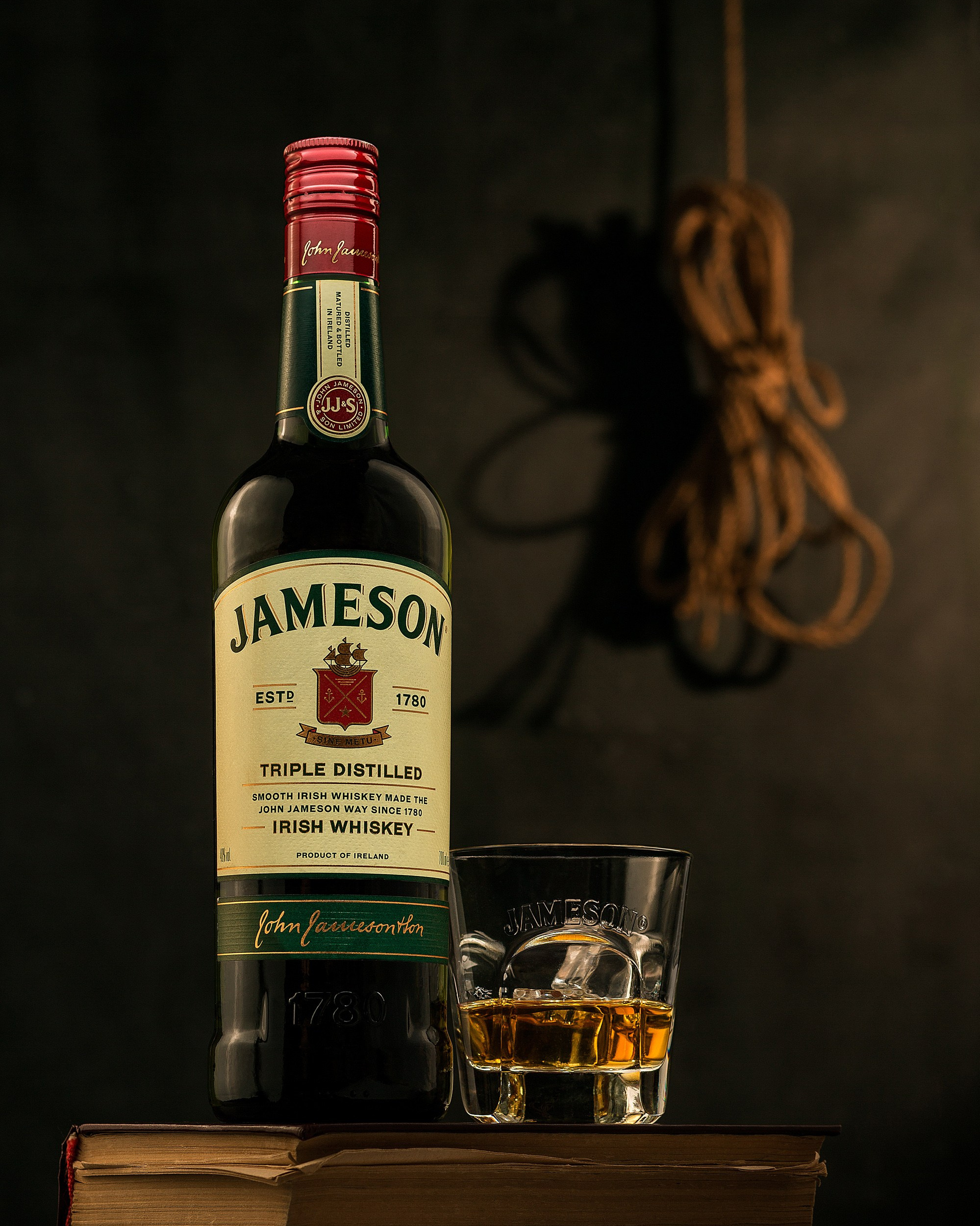 Jameson İrland viskisi şüşəsi və buzlu stəkan köhnə kitabların üzərində, dramatik işıqlandırma ilə studiya çəkilişi.