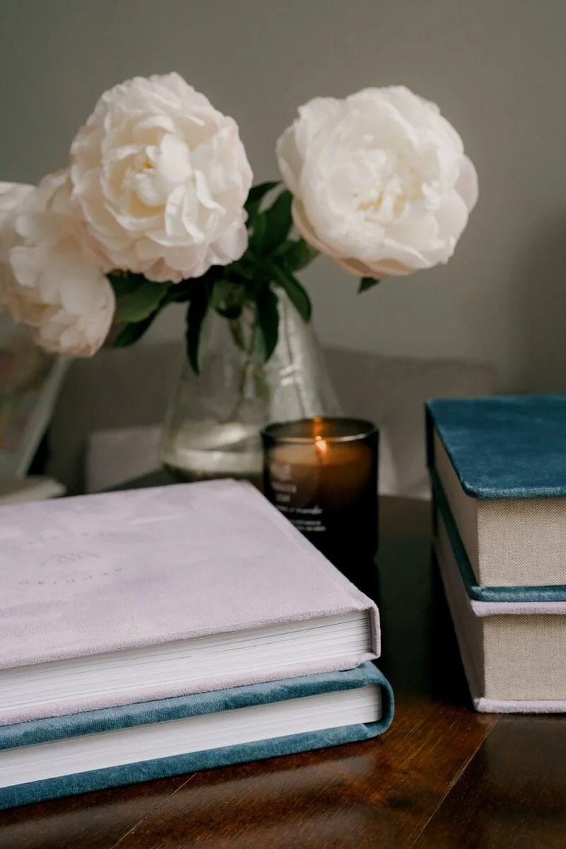 Bridal bouquet in vase beside wedding album and stacked books