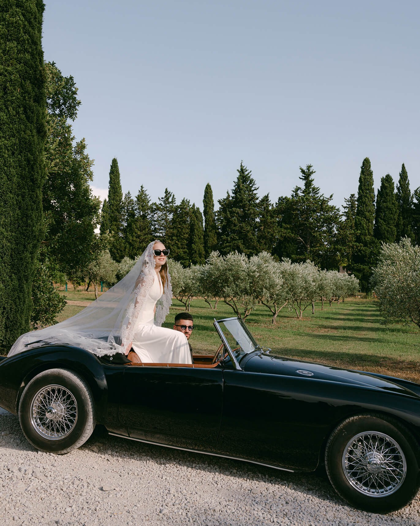 Bride and groom in a vintage convertible, olive grove and cypress trees