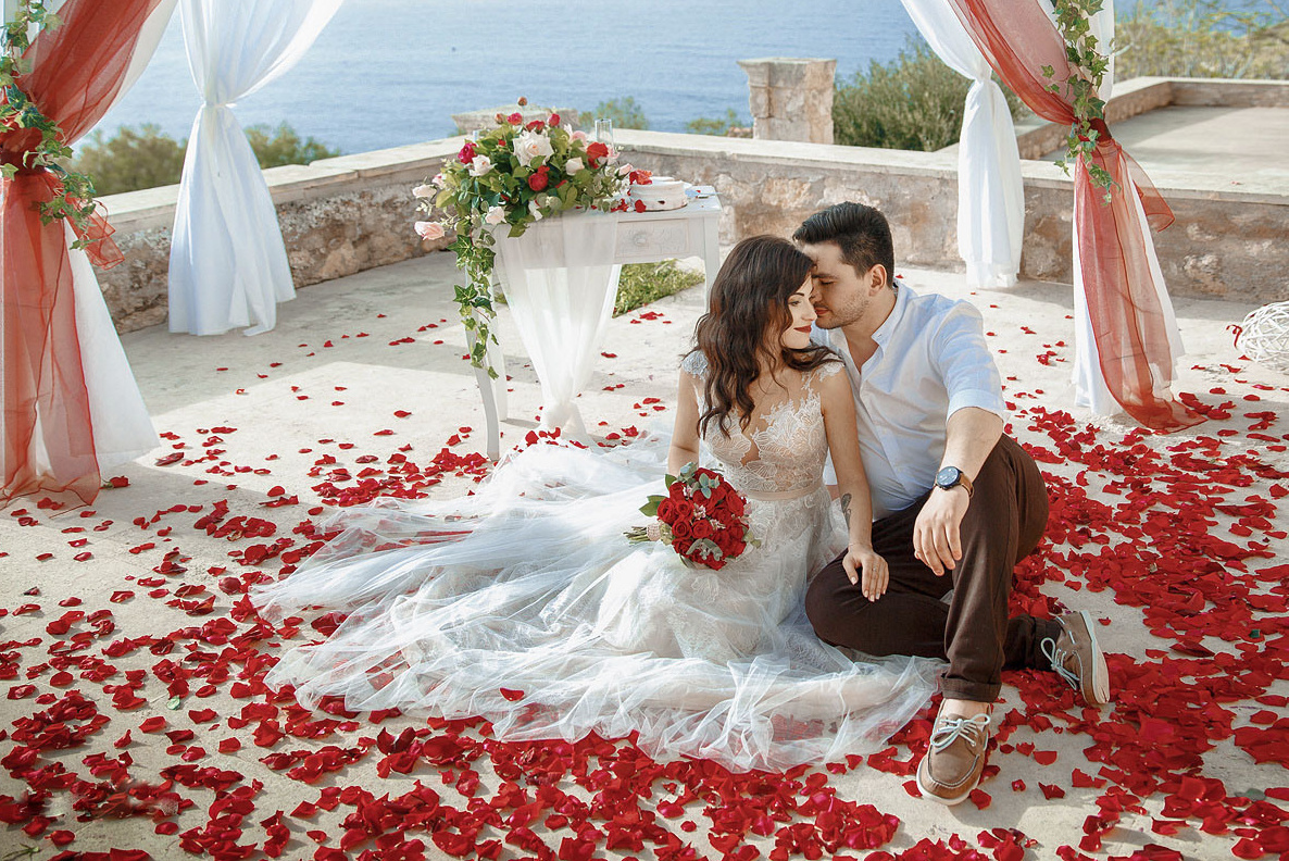 Молодоженов сидят в арке в лепестках роз на Крите. Фотограф, организация свадьбы в Греции.