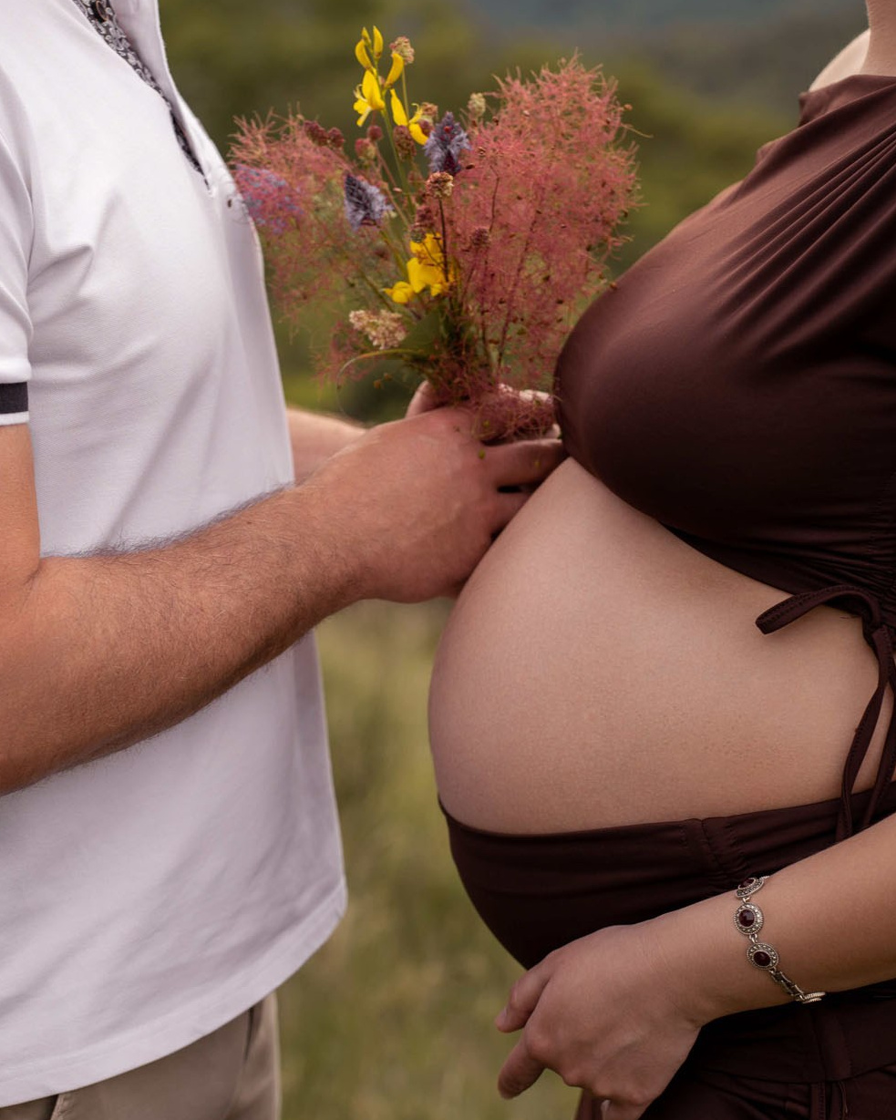Dettaglio delle mani dei futuri genitori sul pancione durante una sessione maternity