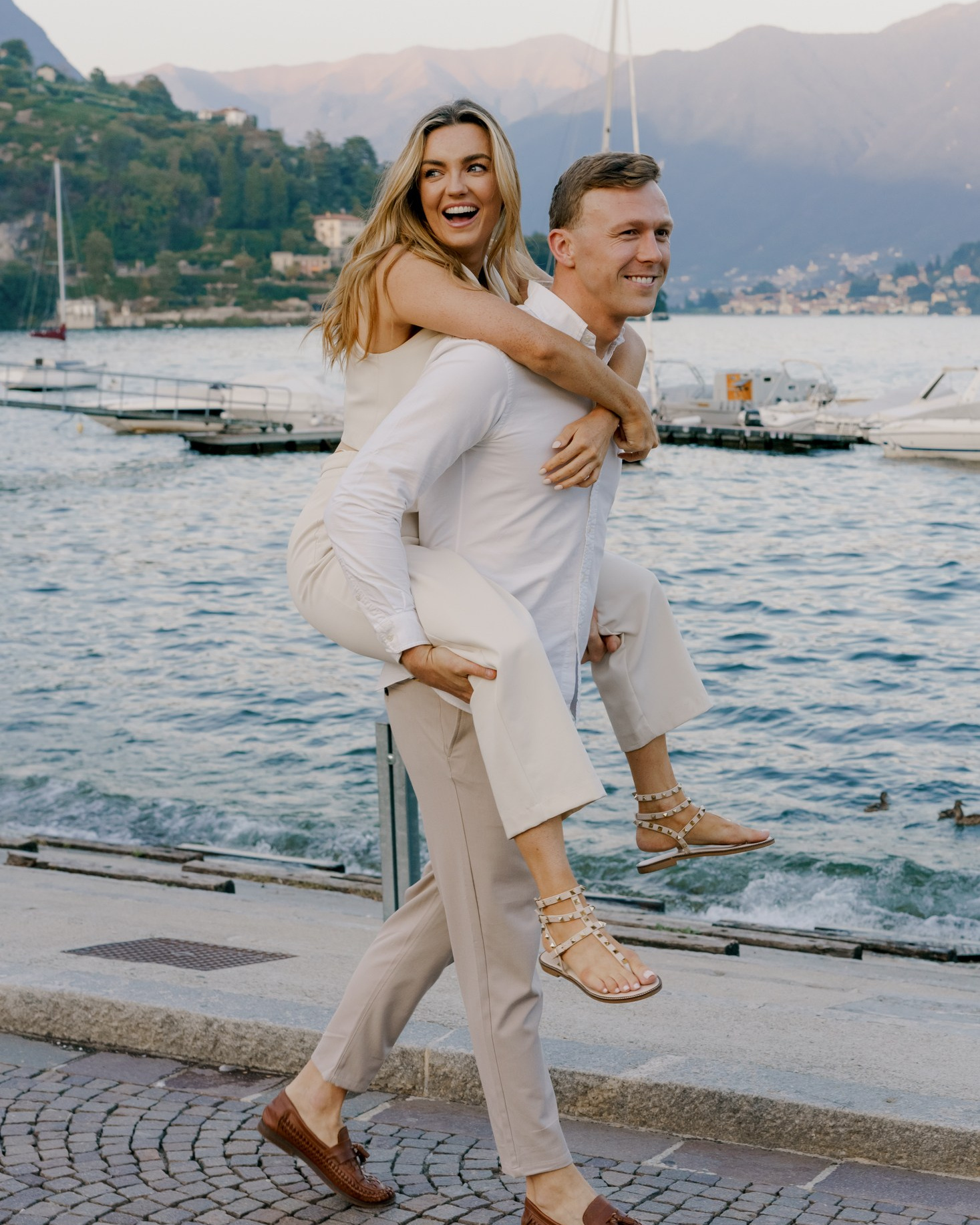 Guy is holding hands of his girlfriend while sitting on the stone and laughing 
