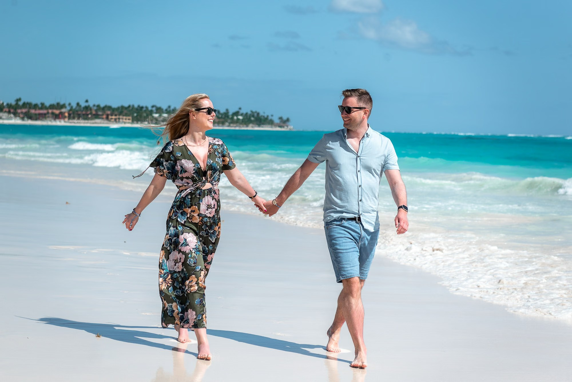 Couple walking hand in hand along the Caribbean shoreline during a romantic Punta Cana photoshoot.