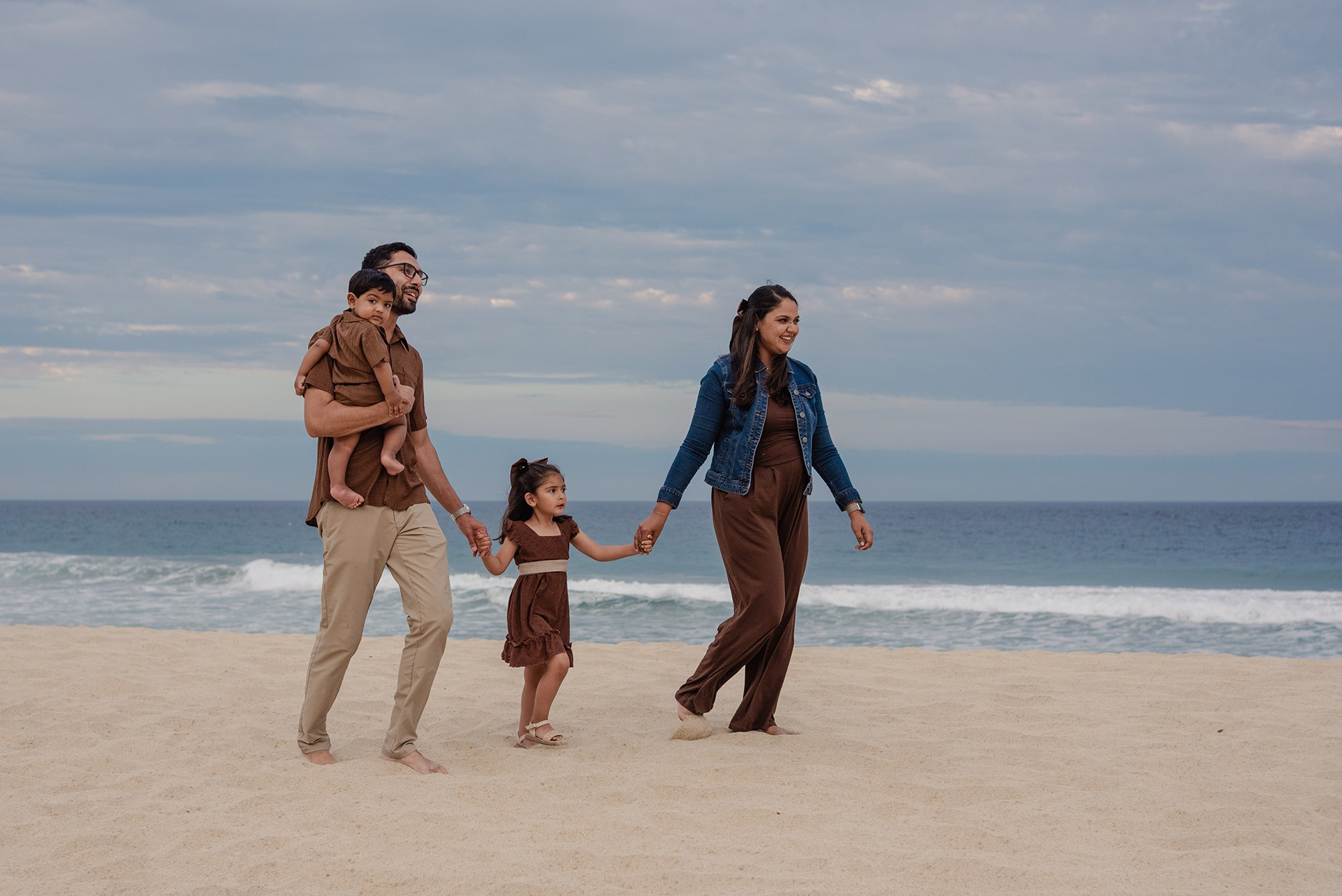 Family walking on a Los Cabos beach dressed in brown and chocolate tones with a denim accent