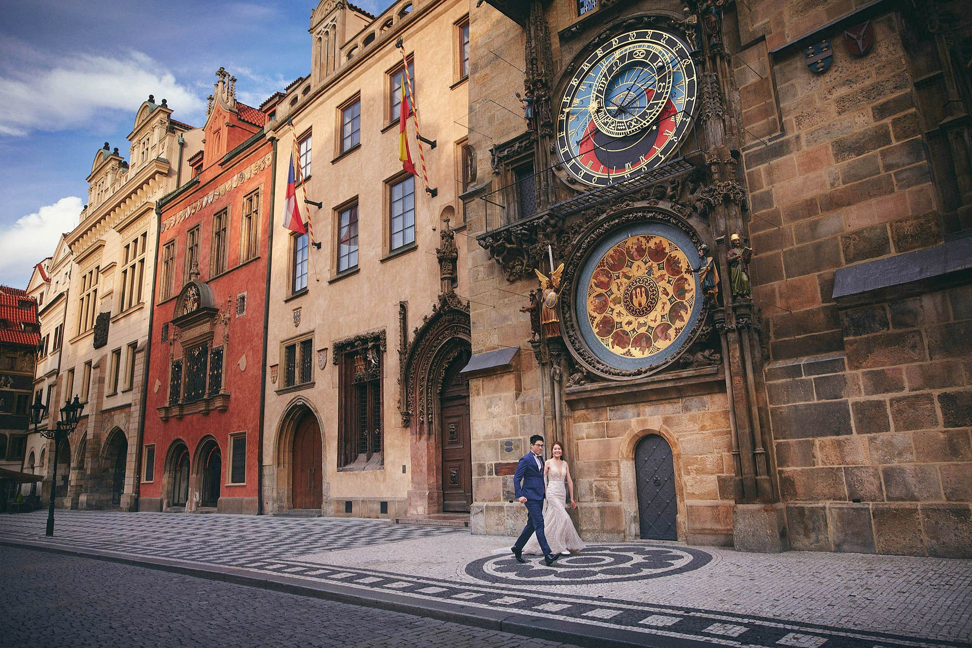 Couple running under Old Town Hall facades toward the Astronomical Clock in Prague.