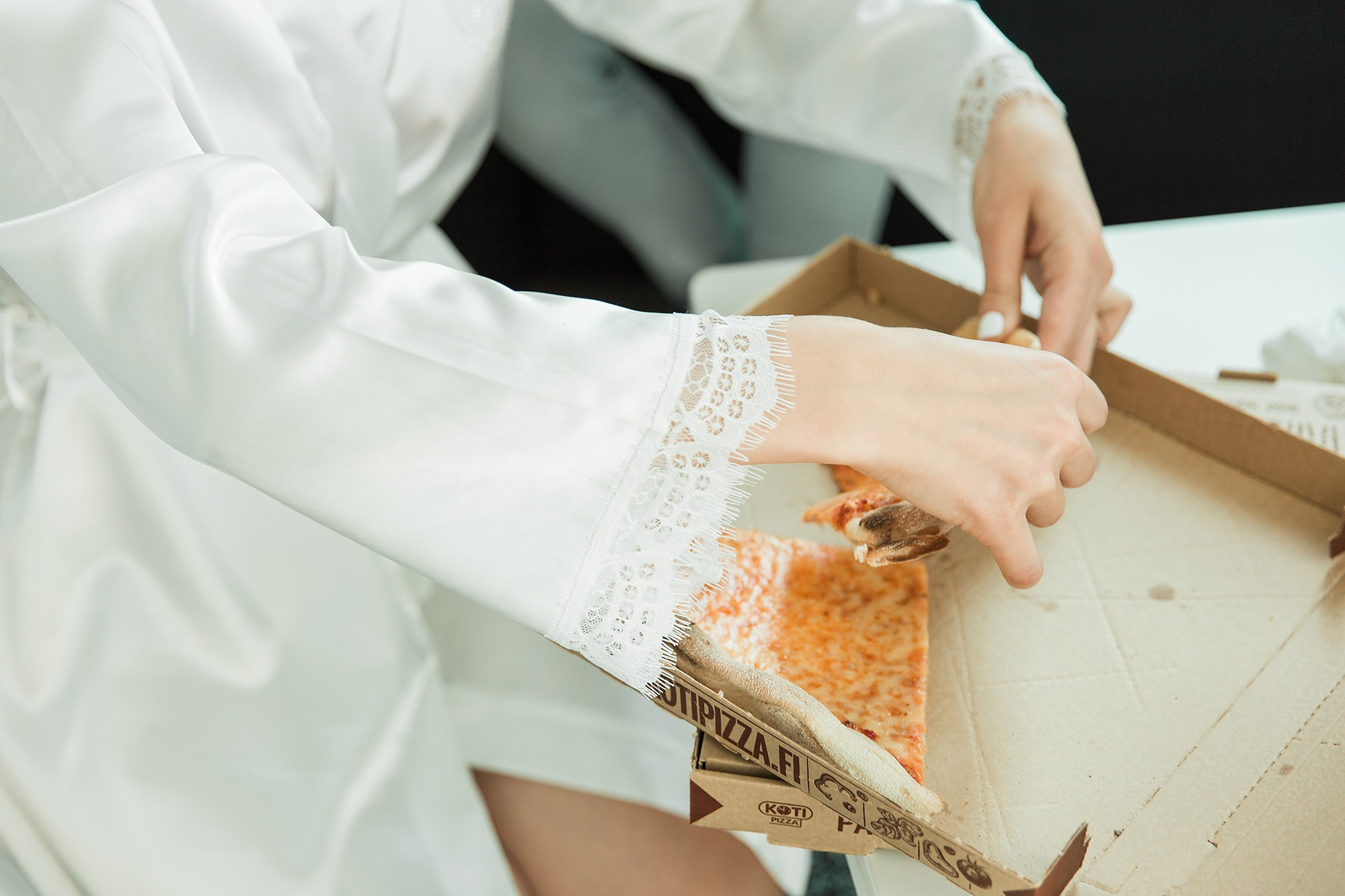 Bride in a silk robe taking a slice of pizza before getting into her wedding dress