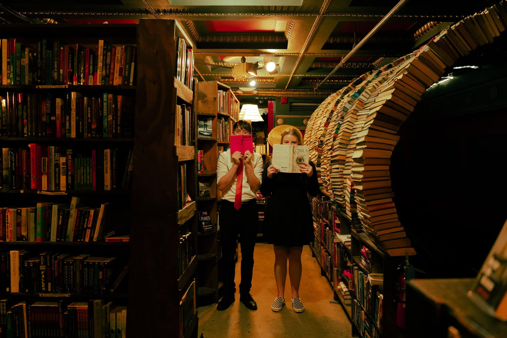Couple standing in front of the iconic tunnel of books at The Last Bookstore, playfully framed by the swirling shelves in this dreamy, cinematic shot