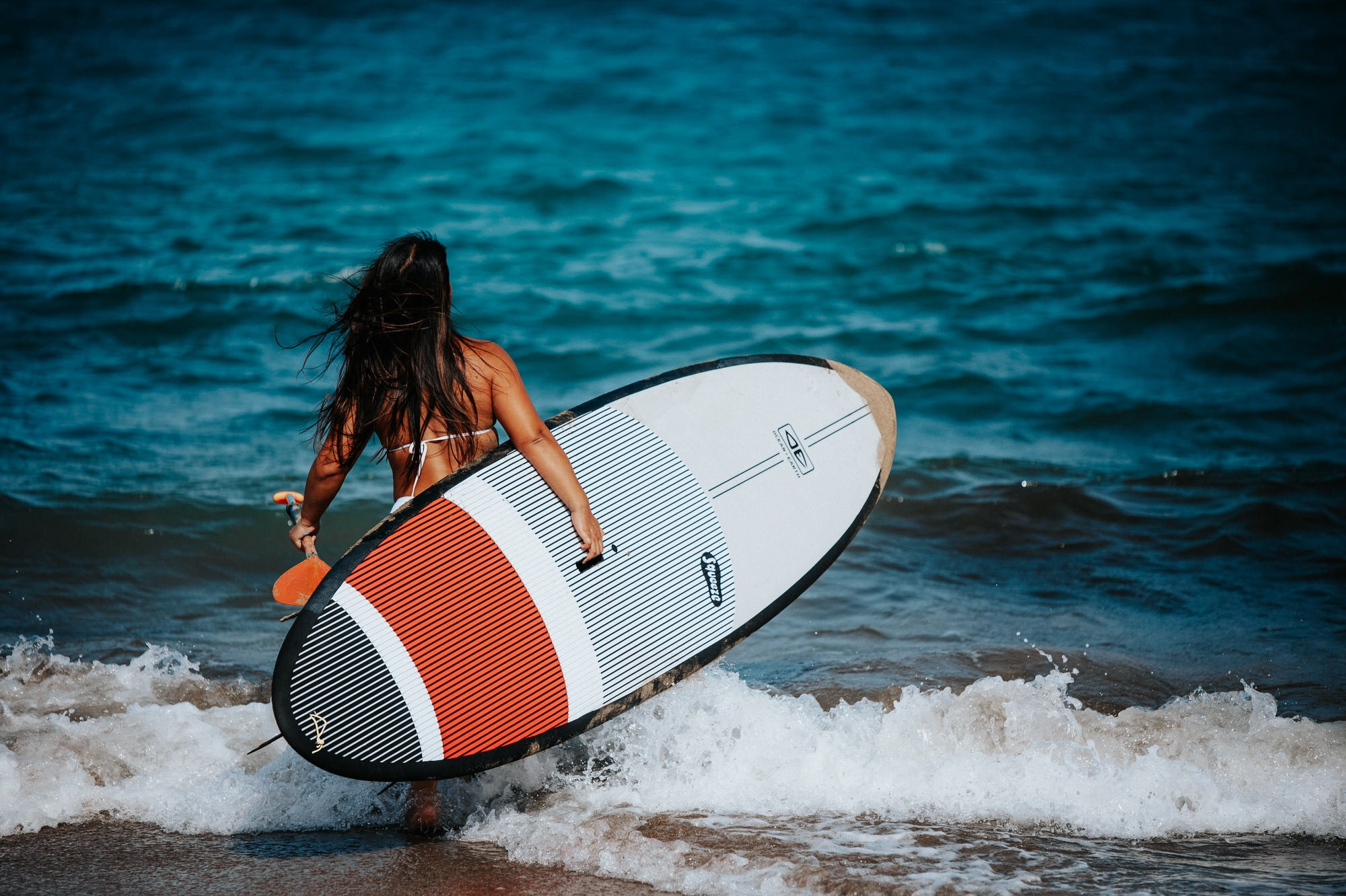 Woman carrying a paddleboard into the Atlantic waves, Gran Canaria
