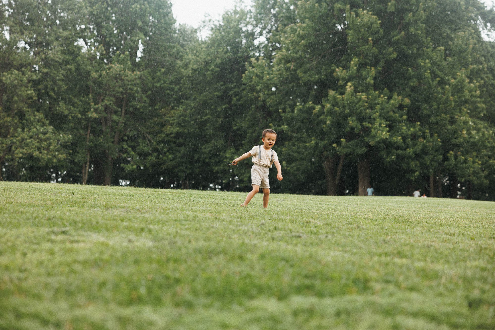 Young boy running across Mount Royal during a rainy family session in Montreal