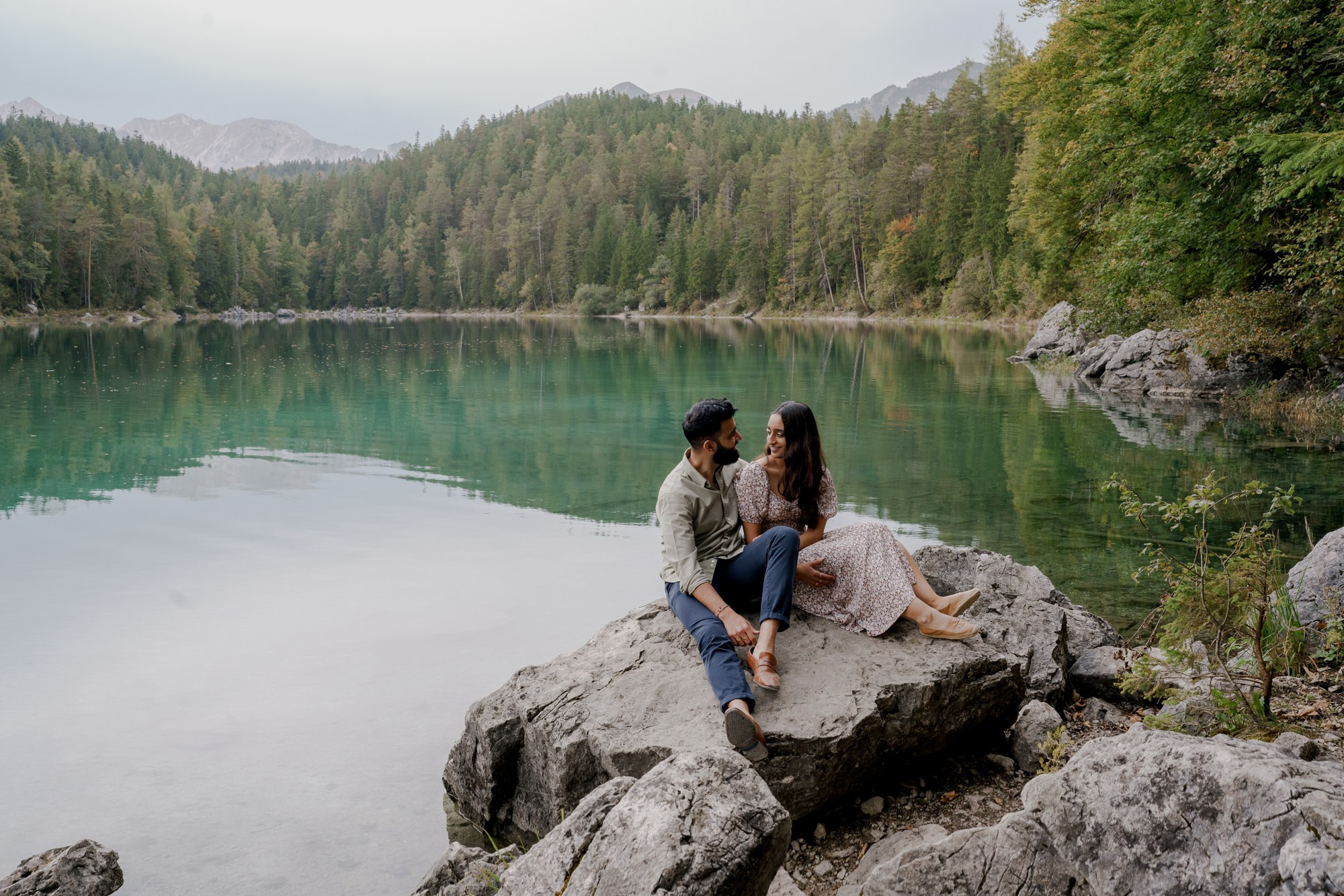 couple is sitting on the rock and looking to each other at Eibsee