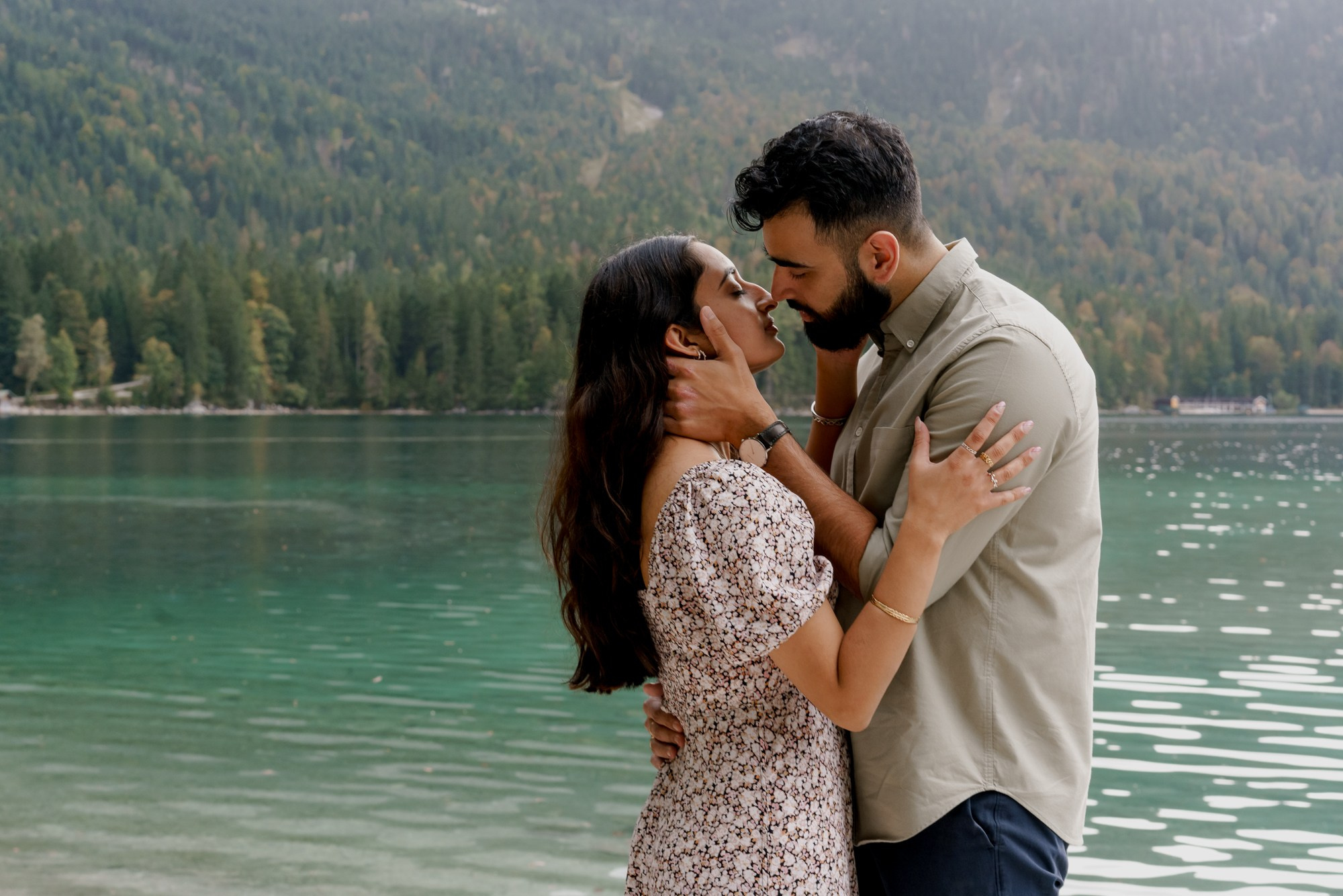 man is touching the face of his future wife with a green water of Eibsee at the background 