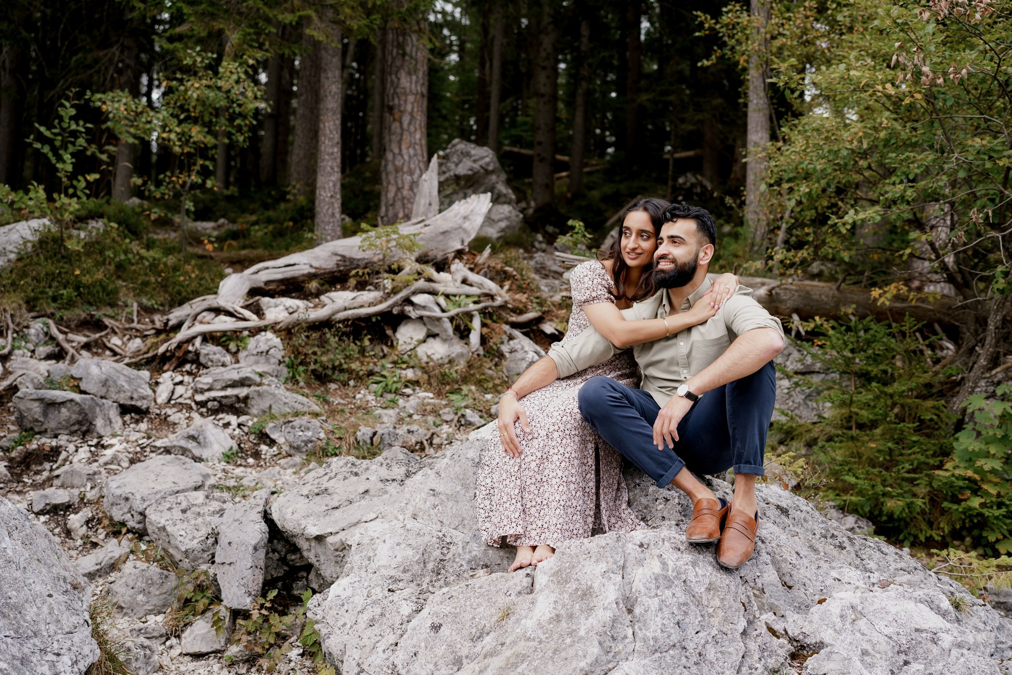 indian couple is sitting on the rock with a forest on the background 