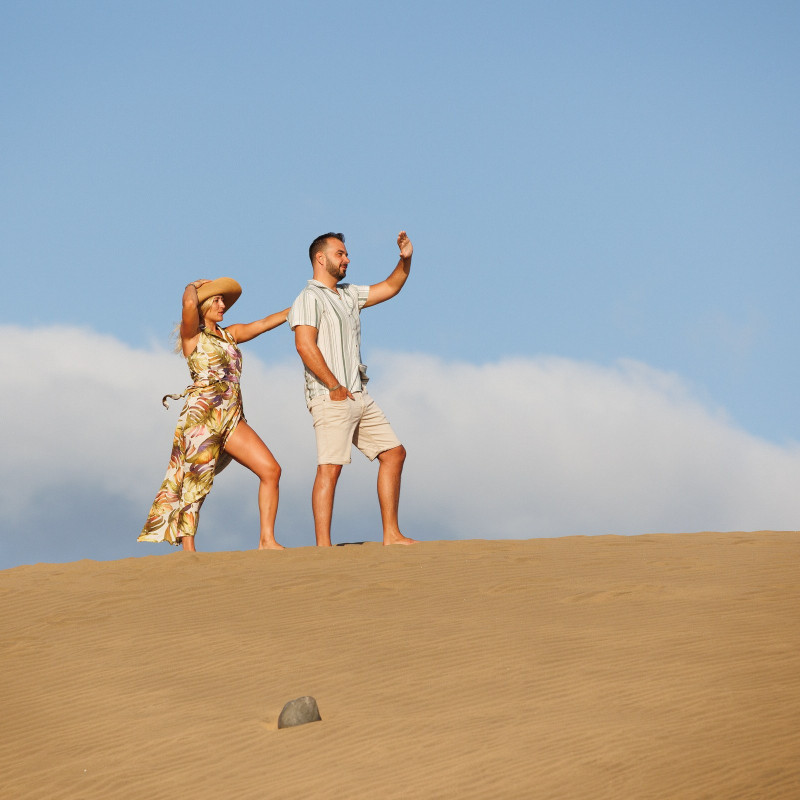 A man and woman walk together on a sandy hill under a blue sky, Maspalomas Photoshoot