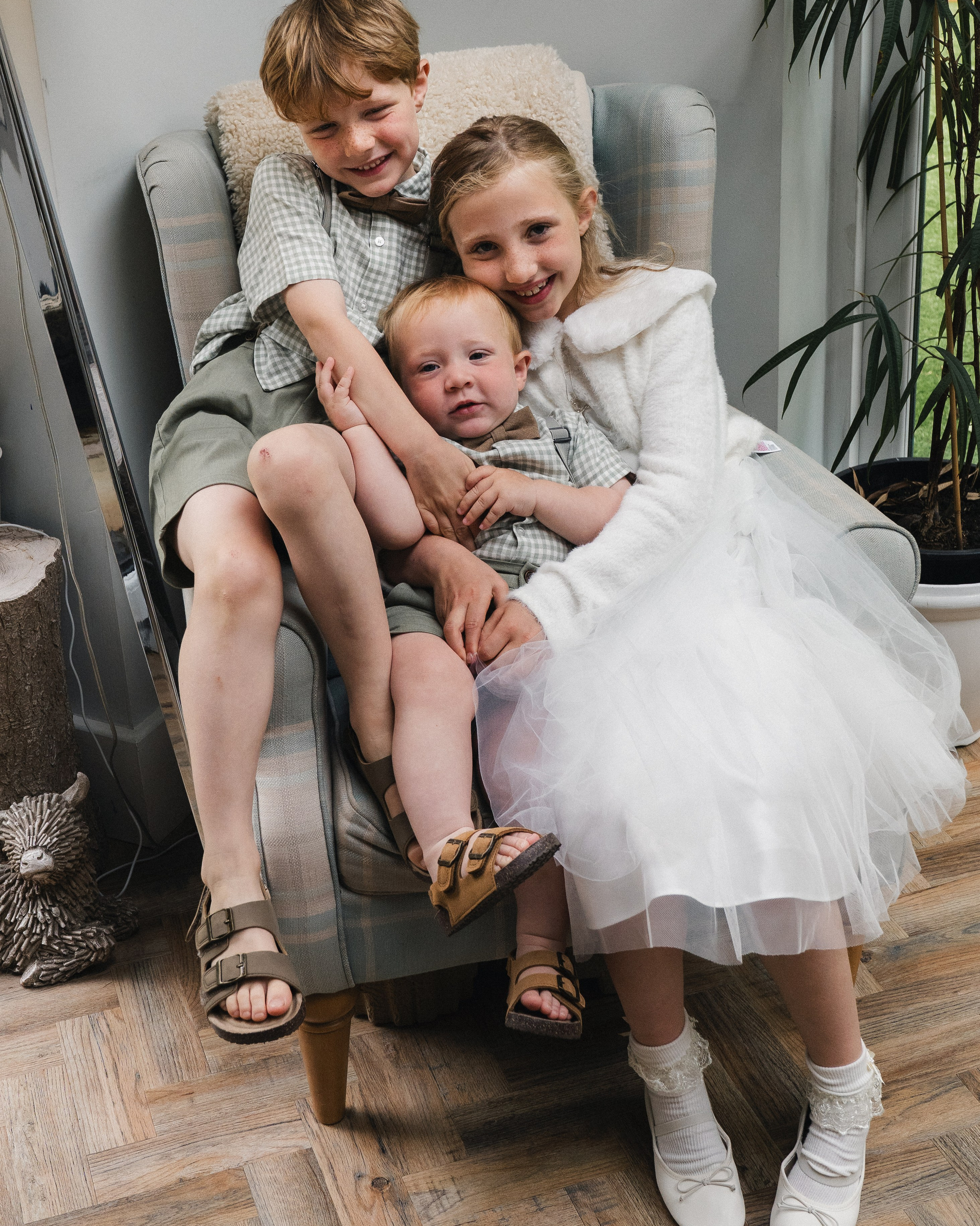 Three siblings cuddling together in an armchair during a relaxed indoor family photography session in Newcastle Upon Tyne.