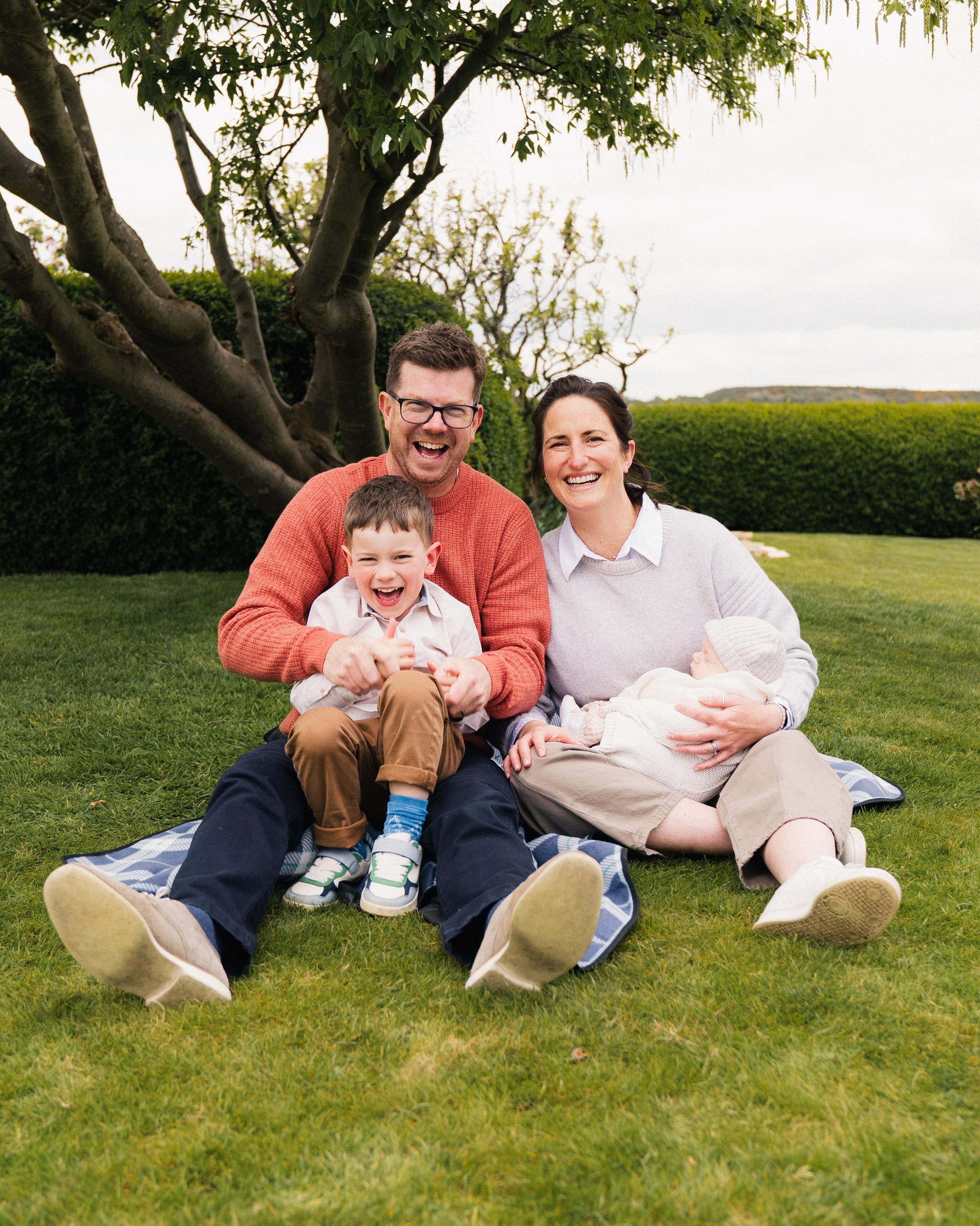 Young family sitting together on a picnic blanket during an outdoor family photography session in Bamburgh, Northumberland.