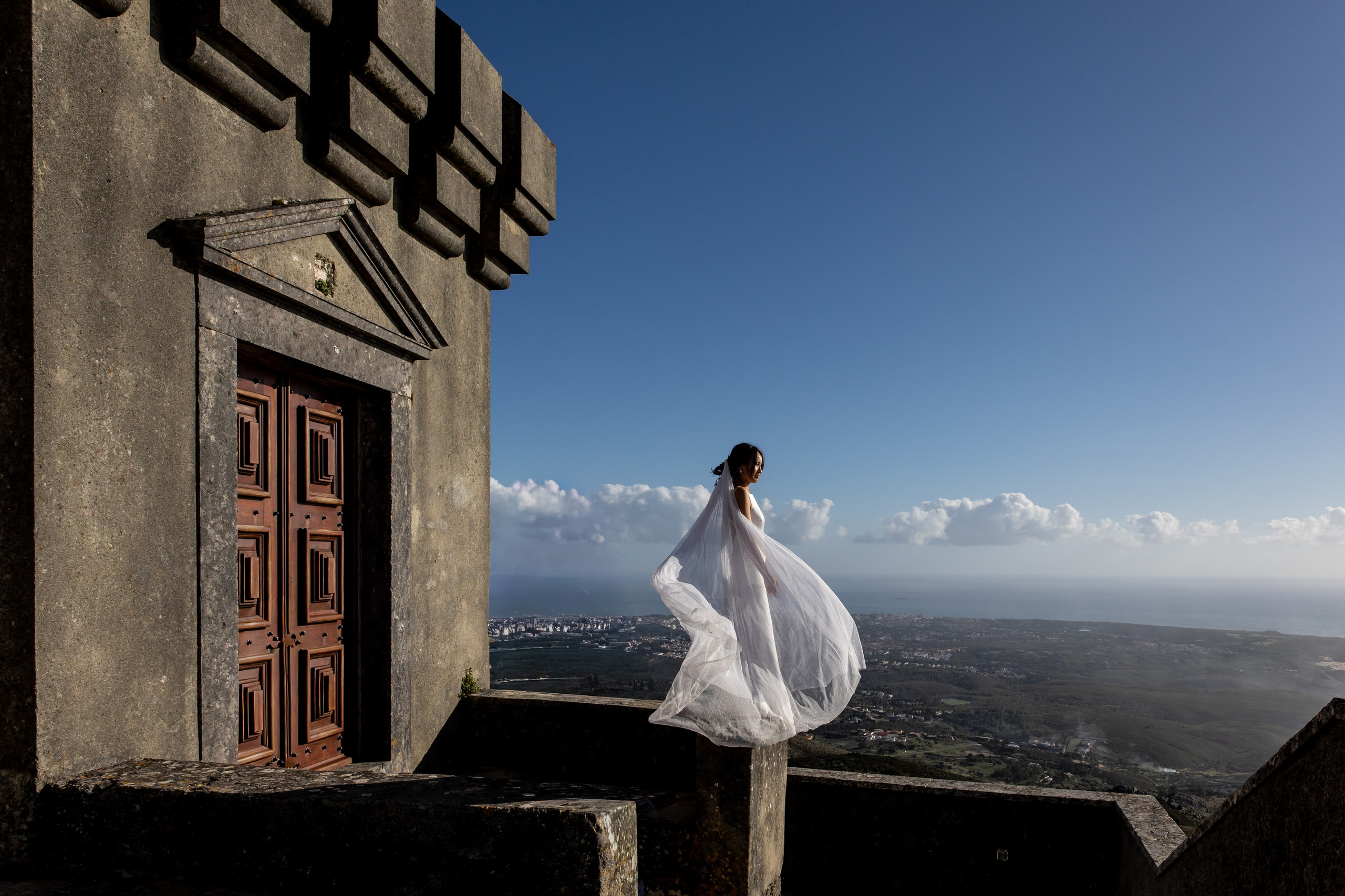 Bride with flowing veil in the wind overlooking the Atlantic during a destination wedding in Portugal