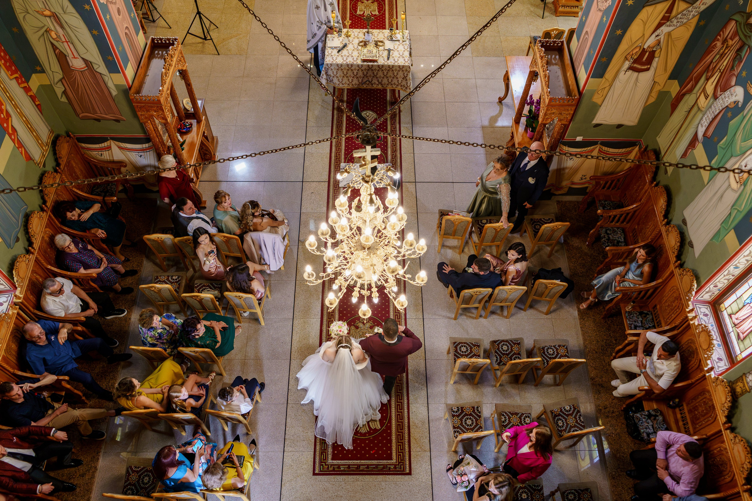 Perspectivă de sus asupra mirilor și invitaților în timpul ceremoniei religioase de nuntă, într-o biserică ortodoxă.