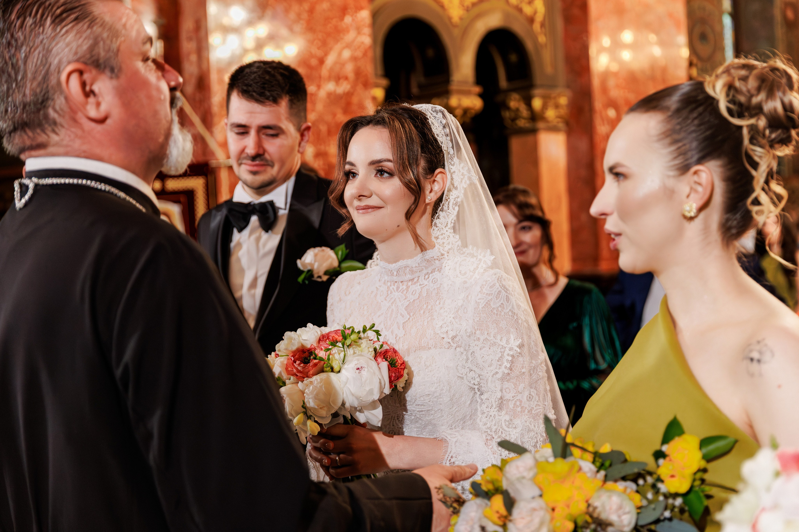 Mireasă privind spre preot în timoul ceremoniei religioase, cu mirele emoționat pe fundal