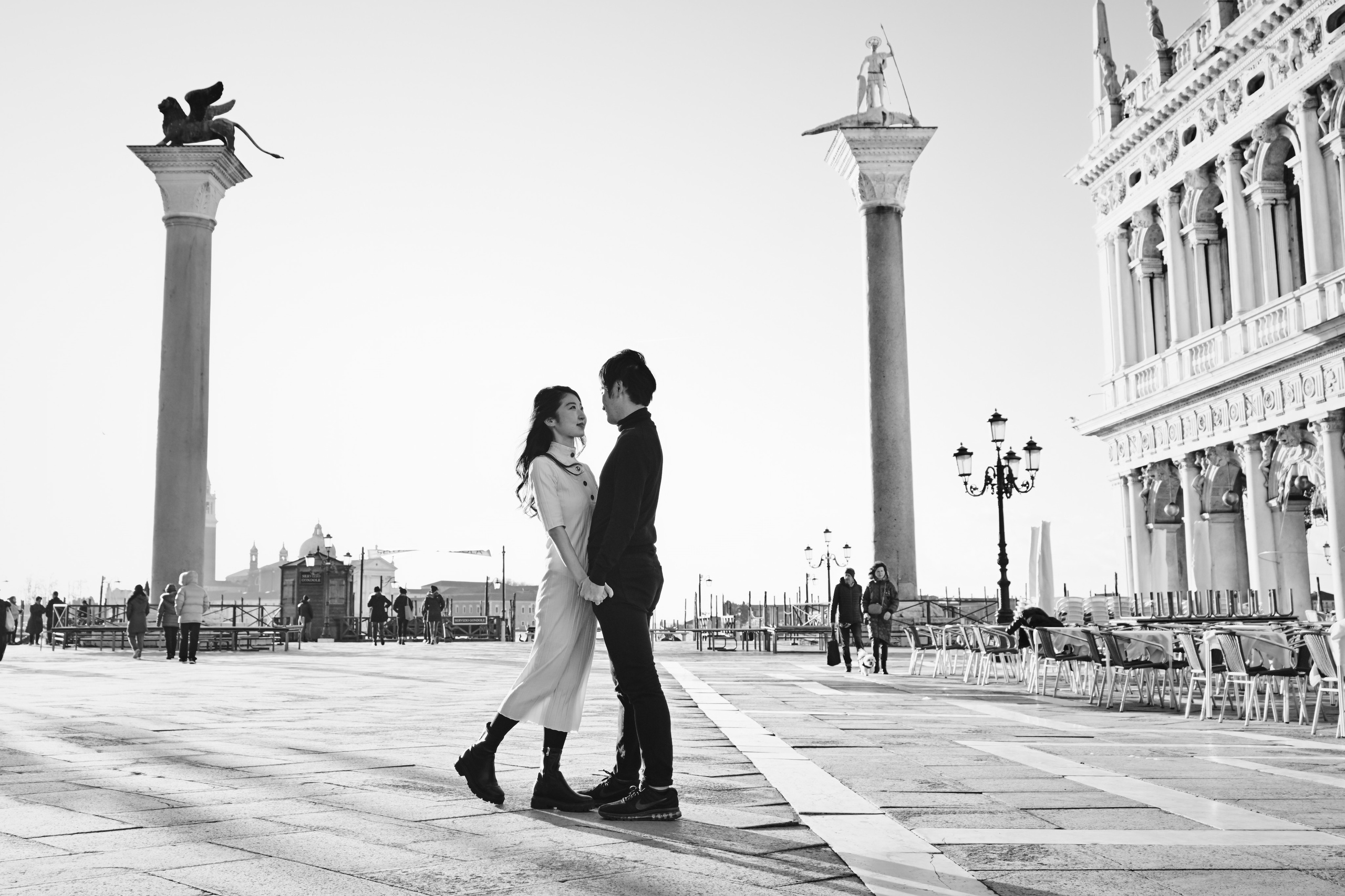 A couple poses for a portrait at San Marco Square, with the Columns of San Marco and San Todaro towering above them. Their love is palpable, and you can feel the excitement of their future together in the air.Sant Mark Square, Italy. In this beautiful portrait photo, a couple stands hand-in-hand, gazing out at the breathtaking panorama of the lagoon and San Marco Square. The intricate details of the surrounding architecture and the warm, golden light of the setting sun create an atmosphere of beauty, love, and passion.