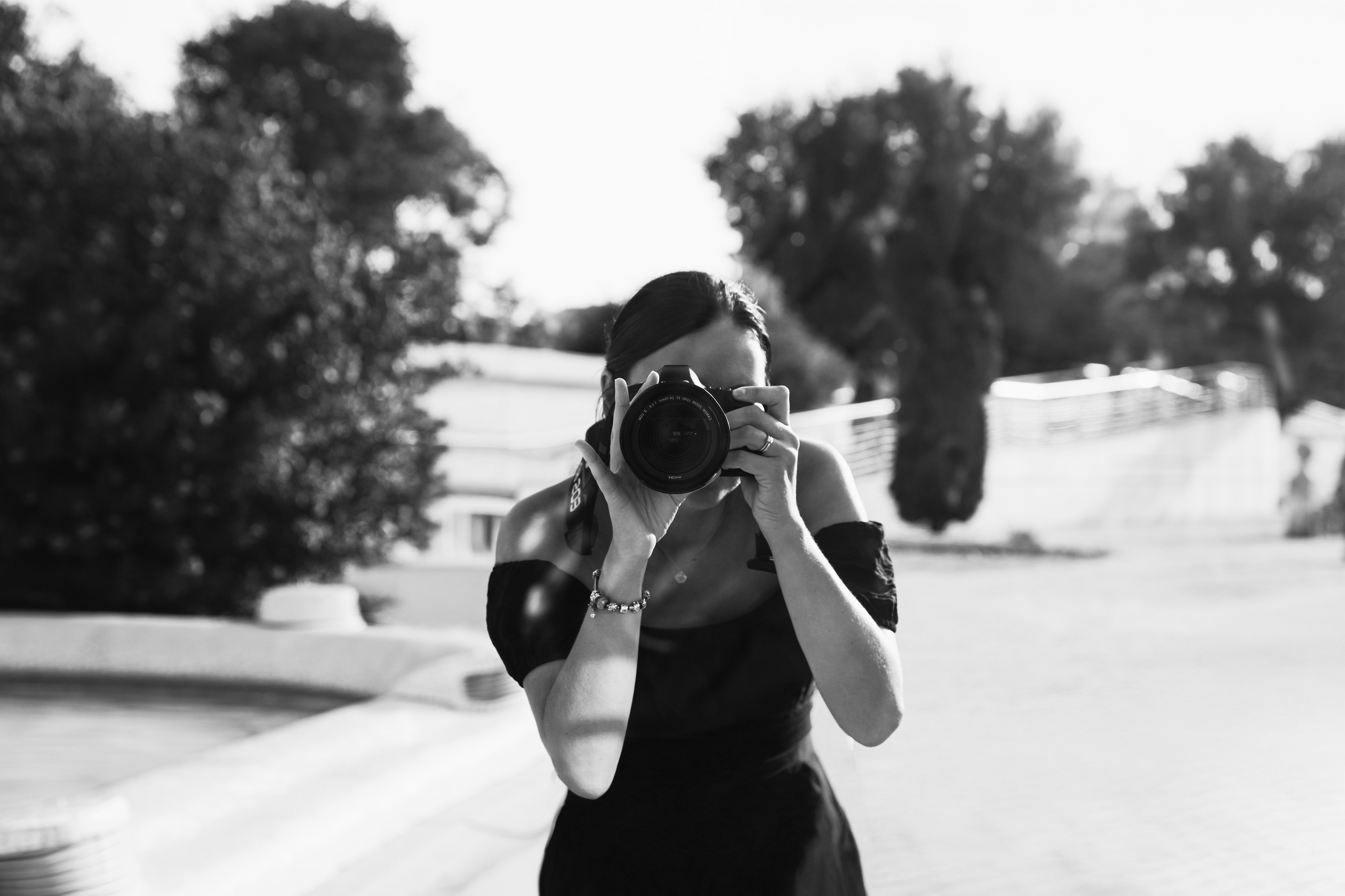 Wedding photographer capturing a candid moment outdoors in Spain, holding a professional camera and smiling naturally. Behind-the-scenes portrait reflecting a documentary wedding photography style and a warm, personal approach.