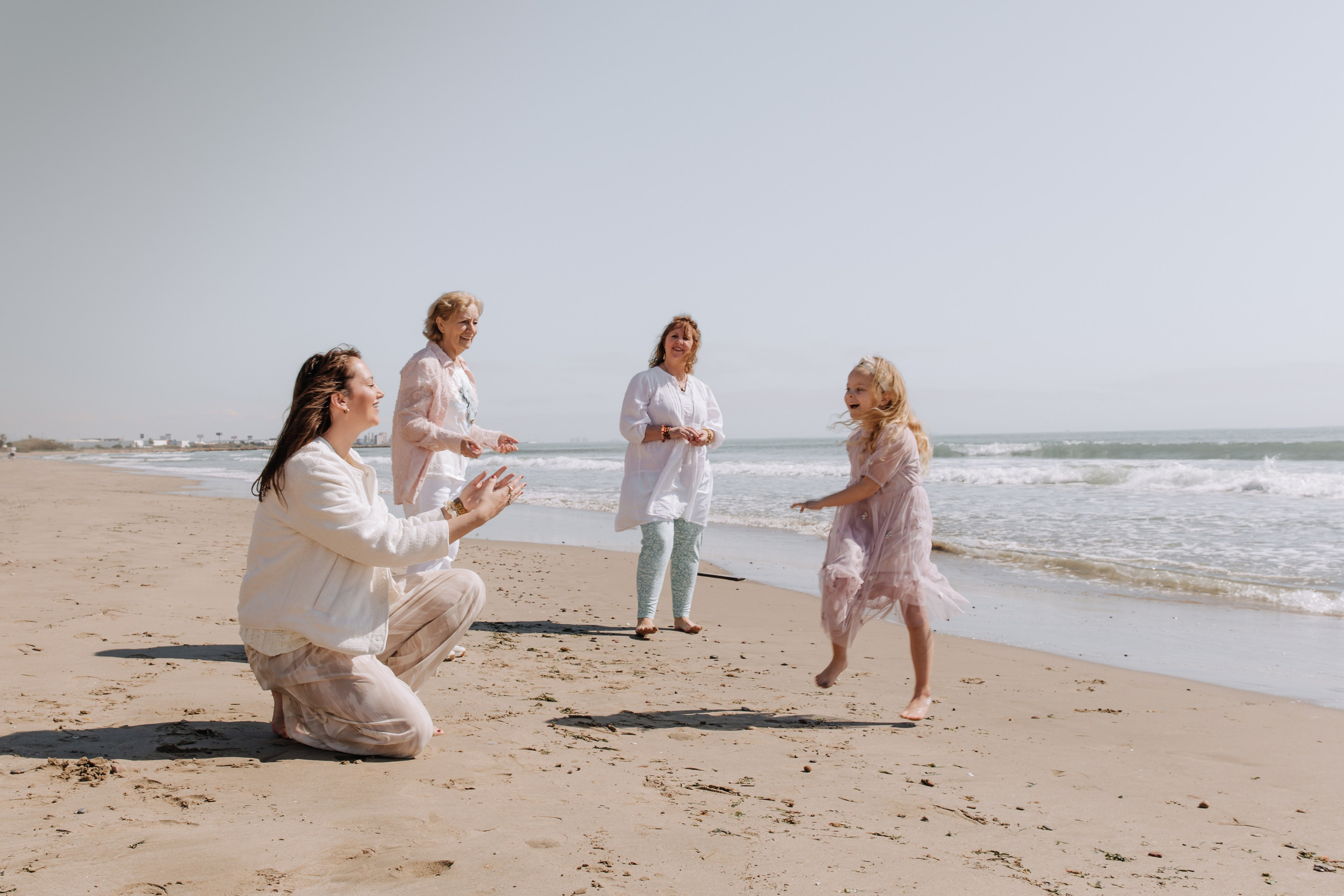 Фотосесія кількох поколінь родини на пляжі у Валенсії, де світлий нейтральний одяг і струмкі тканини дозволяють вільний рух, живу взаємодію та щирі емоції.