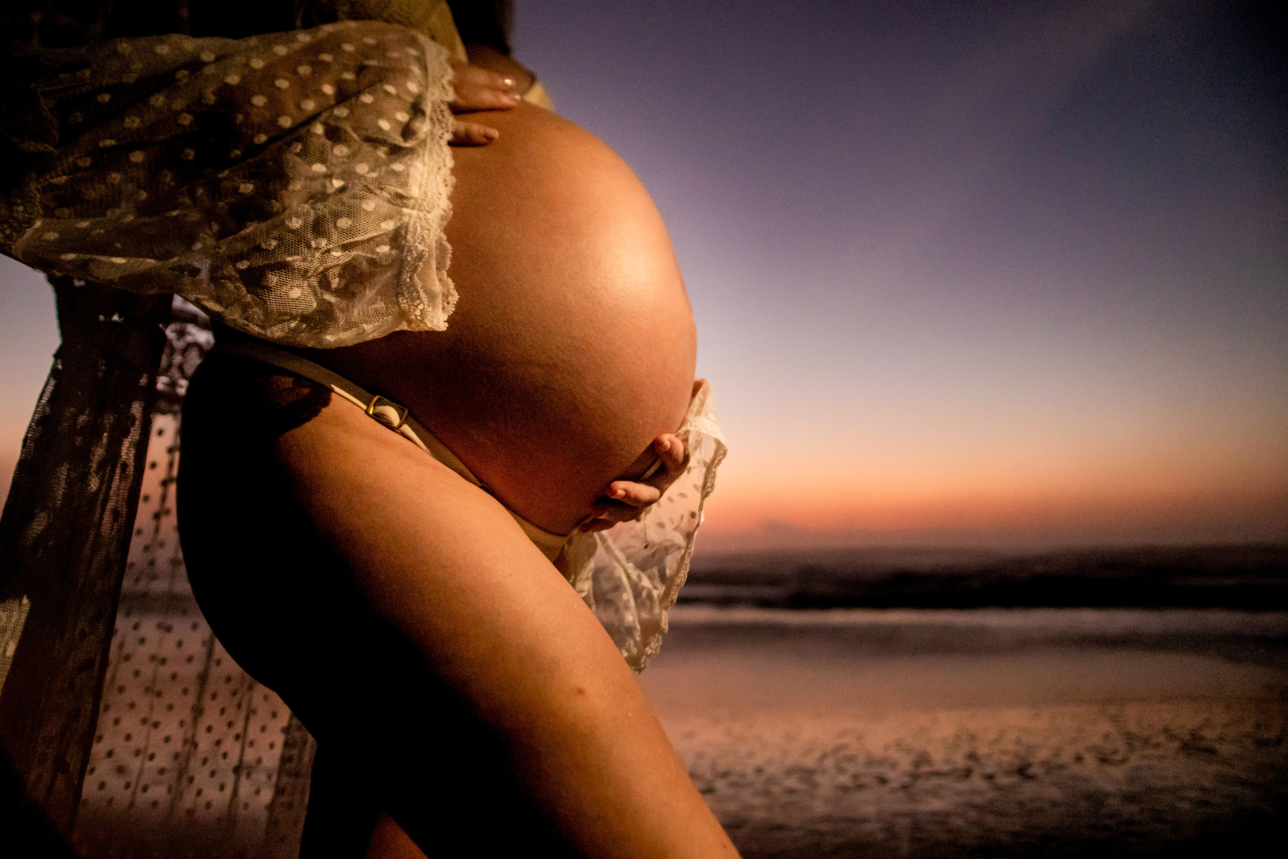 Foto de detalhe da barriga de gestante feito na praia do campeche em Florianópolis-SC no nascer do sol