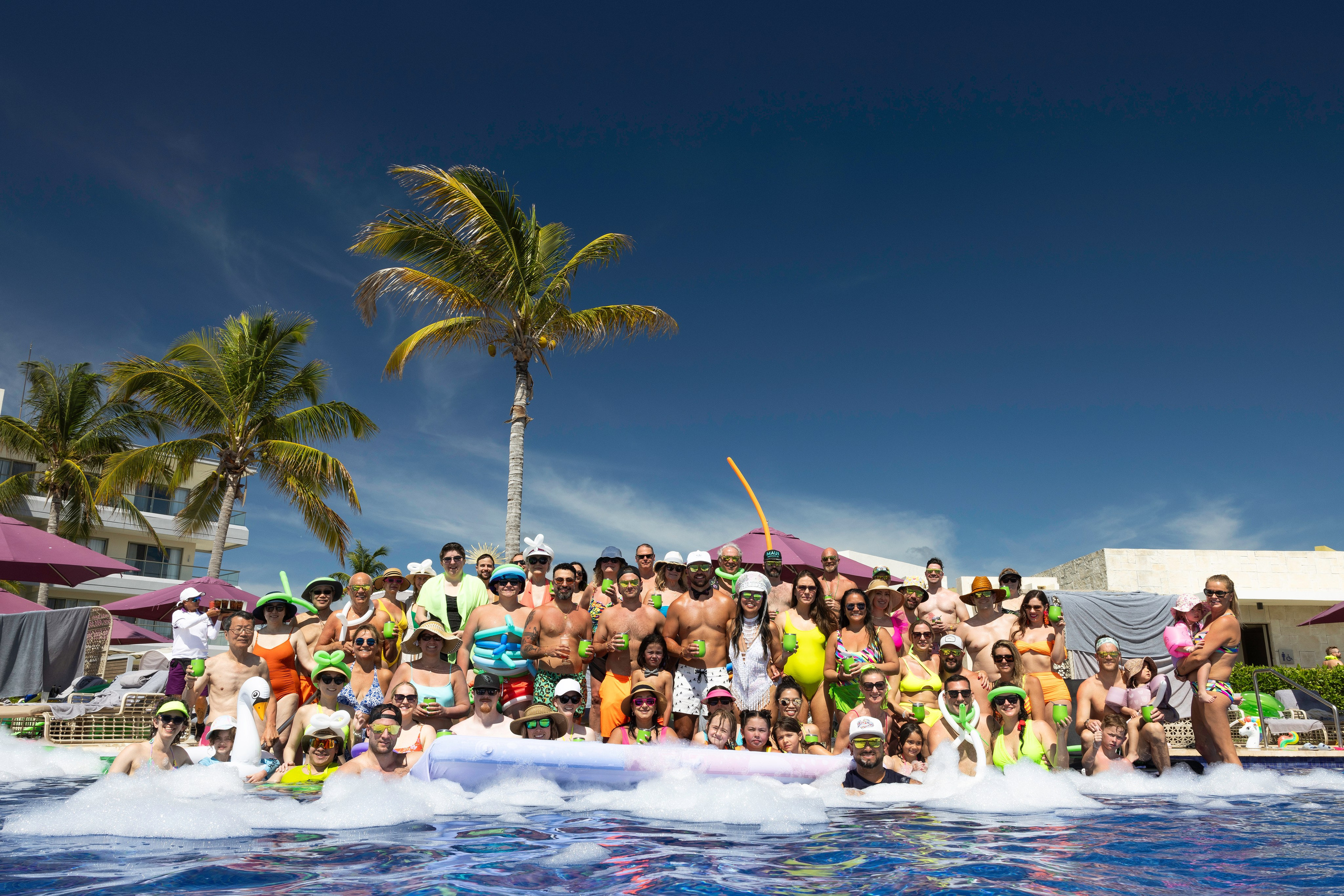 Guests in neon swimsuits cheering during a destination wedding pool ceremony in Mexico.