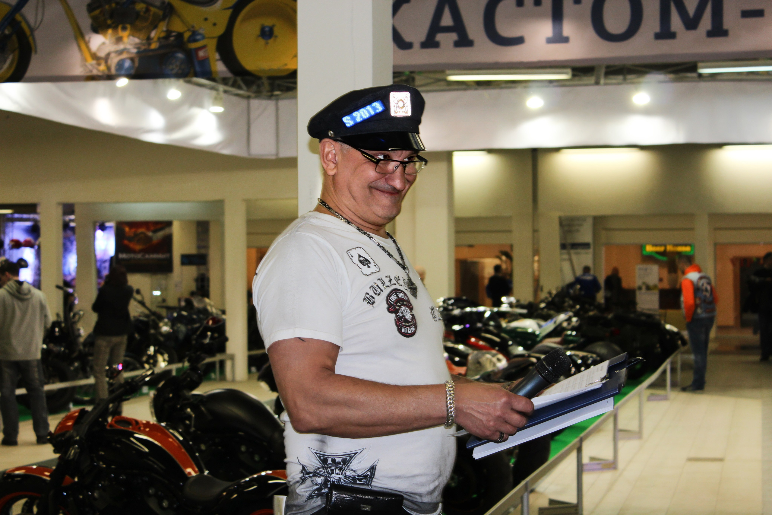 Commercial photo of a cheerful event host in a white t-shirt and leather cap at the exhibition
