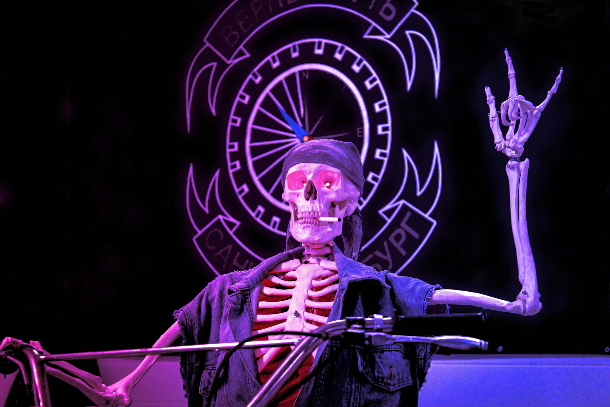 Advertising stand of a sports motorcycle club featuring a skeleton with glowing eyes, a cigarette in its mouth, and making the 'rock on' hand gesture