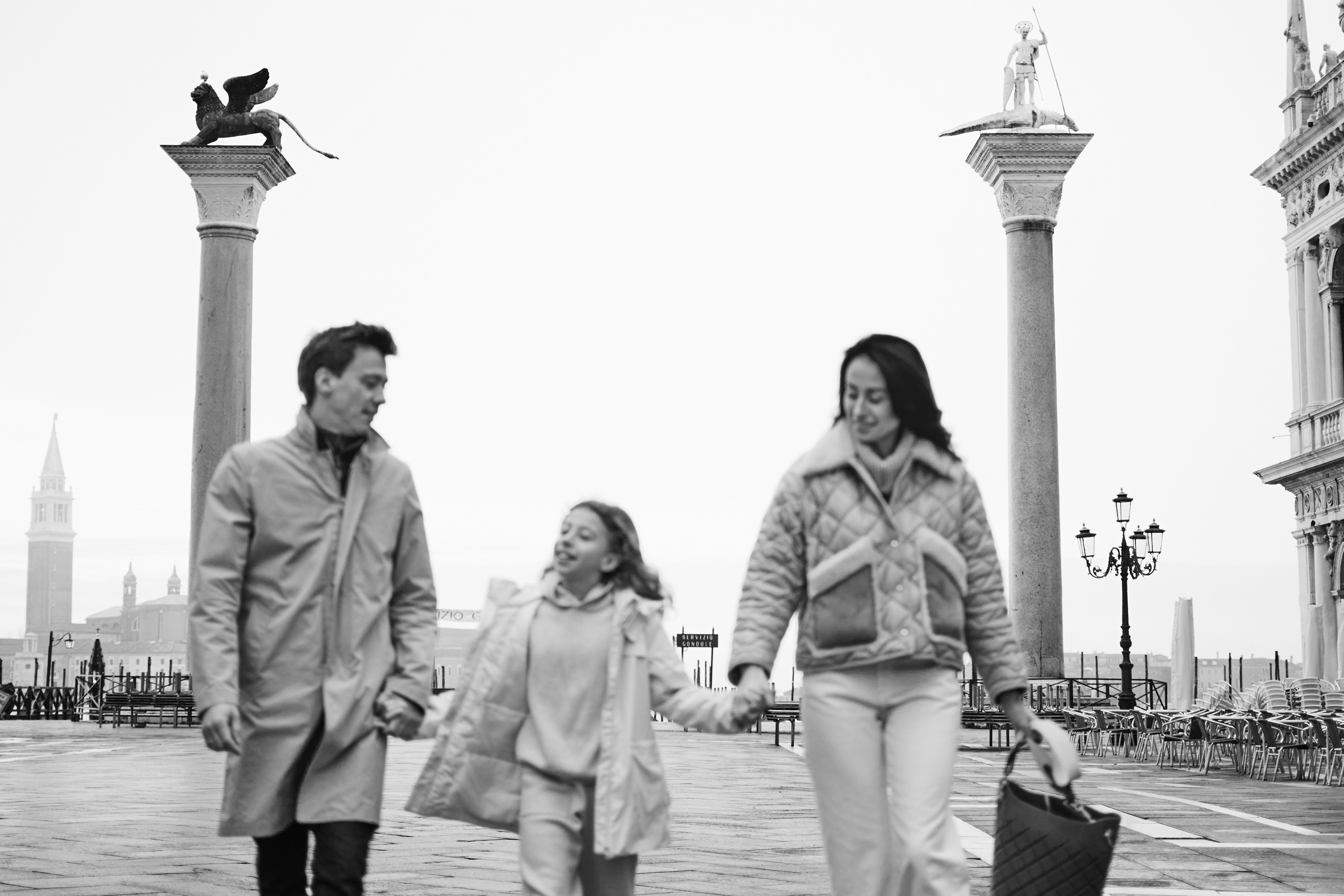 The family stand  in front of the Columns of San Marco and San Todaro, their eyes locked in a passionate gaze. The beauty of Venice surrounds them, and they know that they will always cherish this moment together. Italy, photographer of Venice, family photoshoot