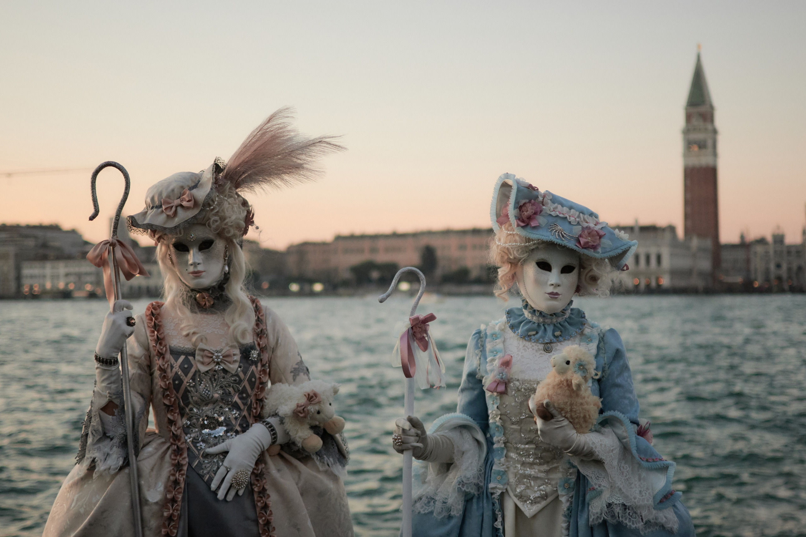 A colorful and lively scene depicting people wearing elaborate masks and costumes, walking along the historic streets and bridges of Venice during the Carnival celebration. Vibrant hues, intricate designs, and a festive atmosphere characterize the image.