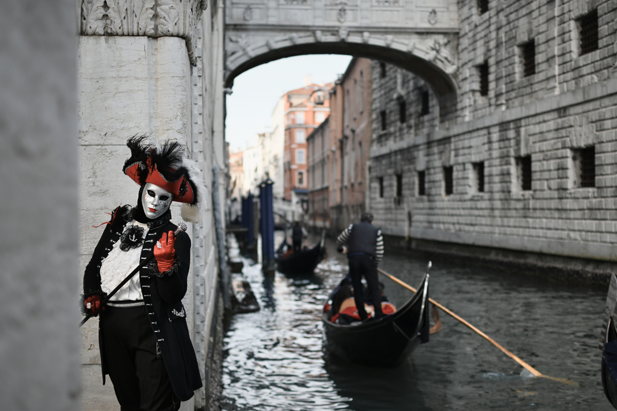 A woman wearing a mask and costume with feathers and glitter posing on a gondola. Bridge of Sighs on San Marco square in Venice, Italy