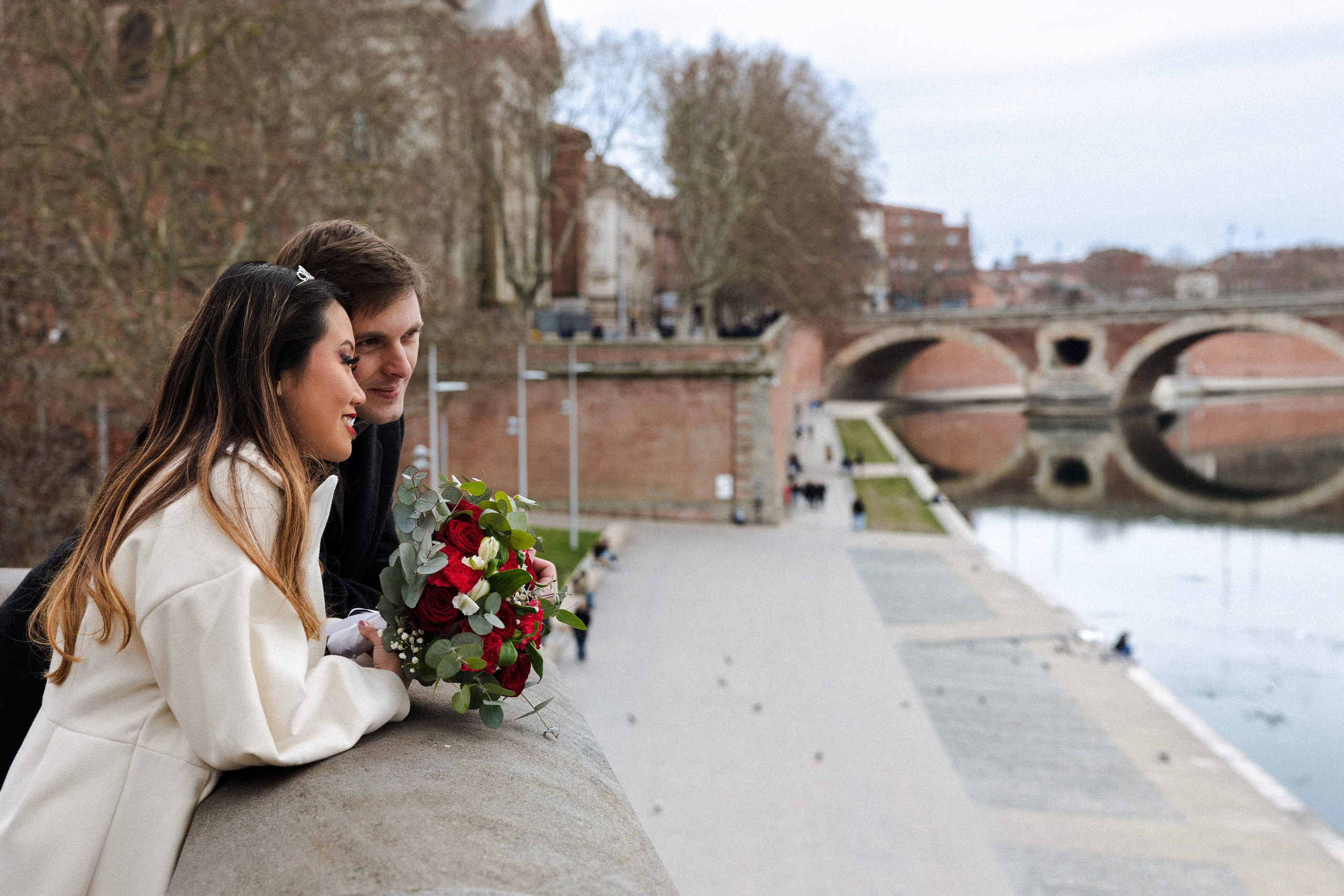 Bride holding a bouquet on the Garonne quay beneath a stone arch bridge in Toulouse