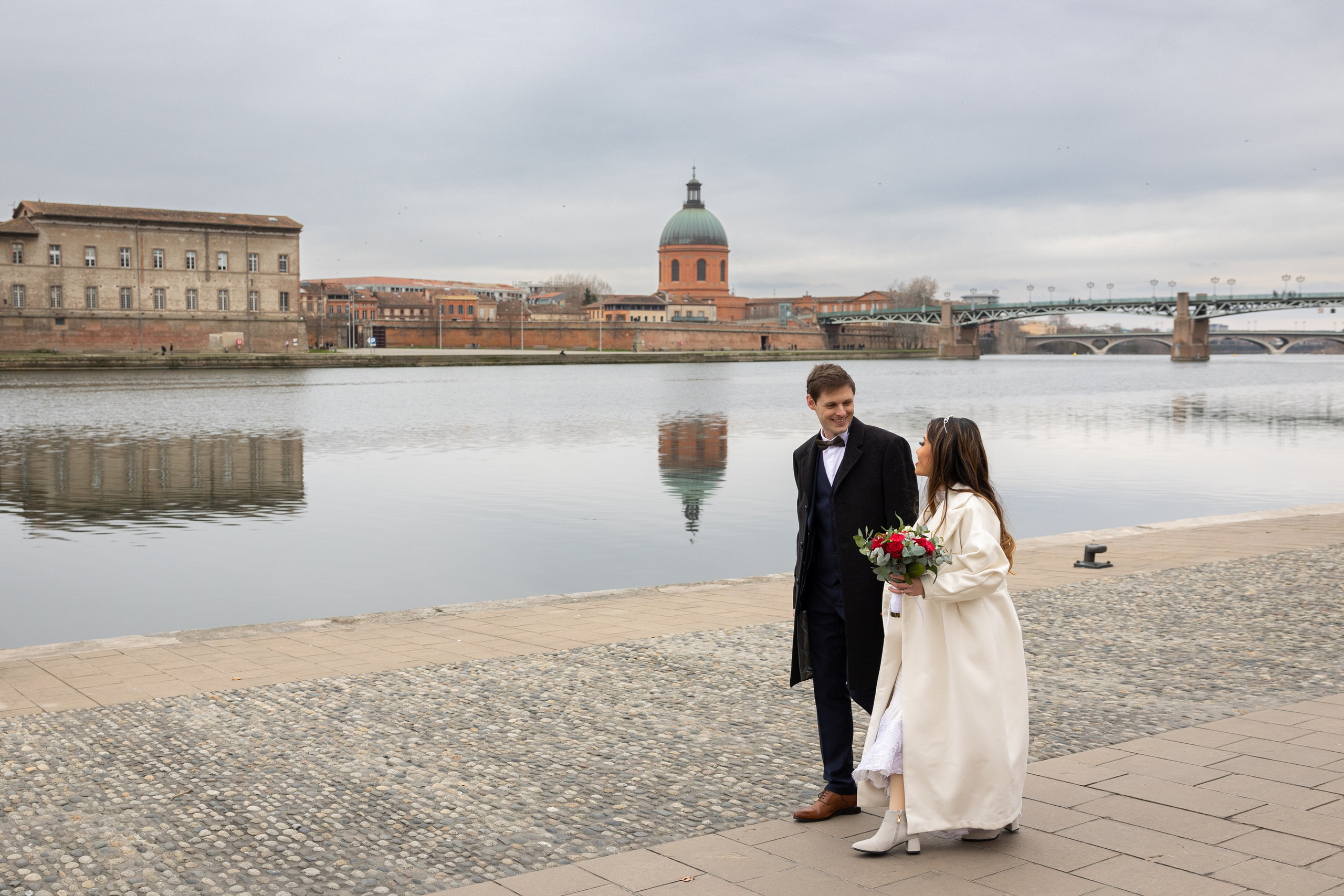 Couple standing by the Garonne river with Pont Neuf and the Toulouse skyline behind them