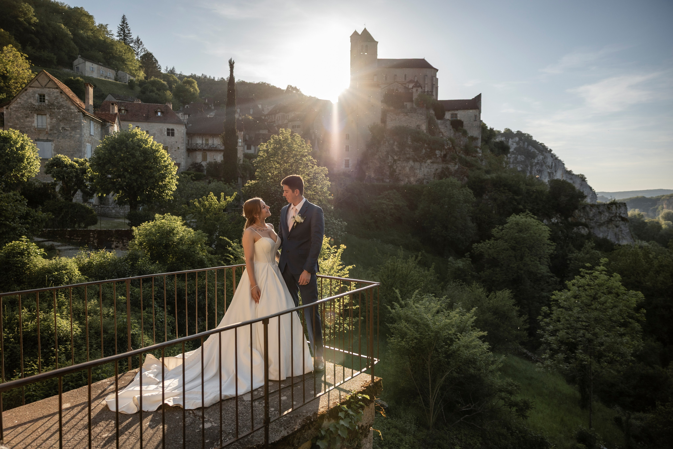 Bride and groom on a terrace above a hilltop medieval village at sunset, Southwest France