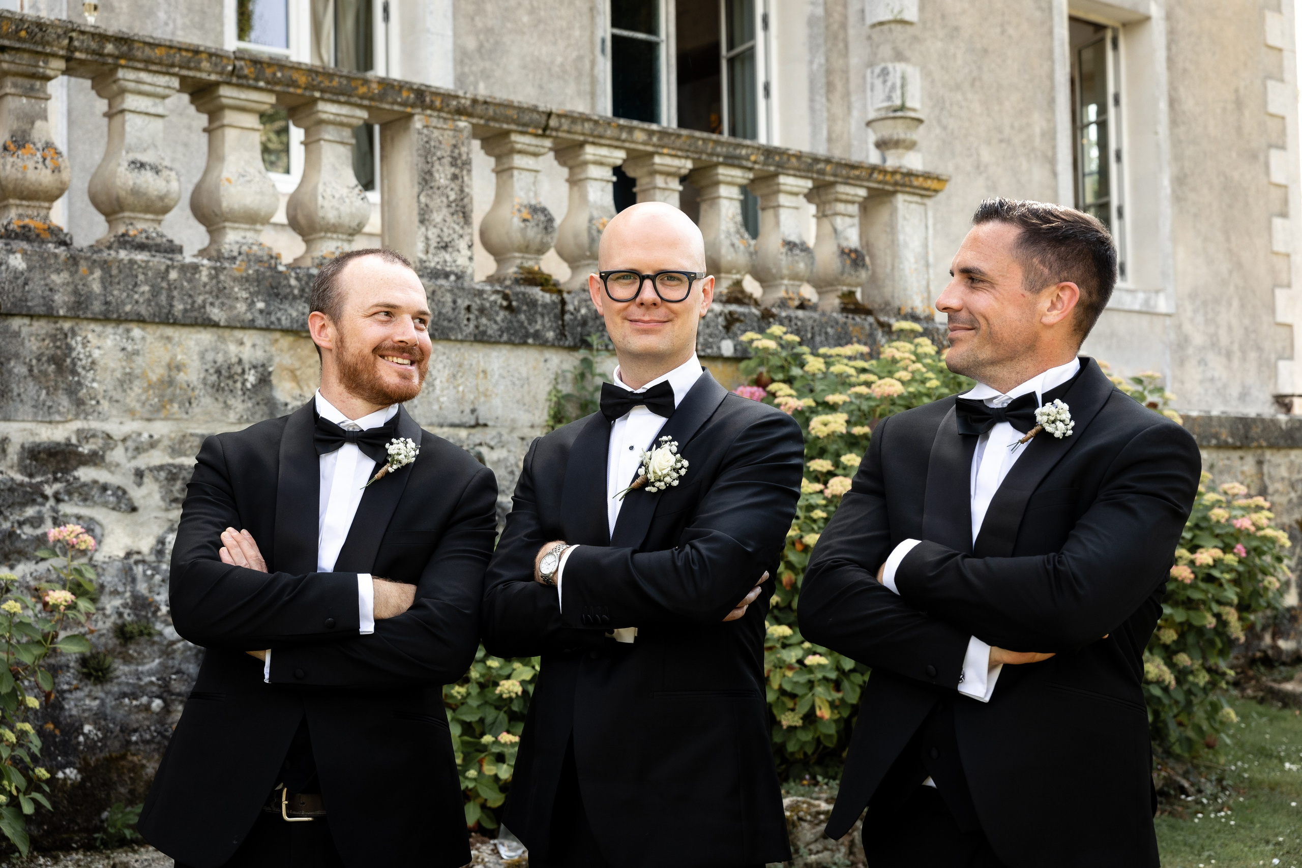 Three men in black tie by the stone balustrade outside the château