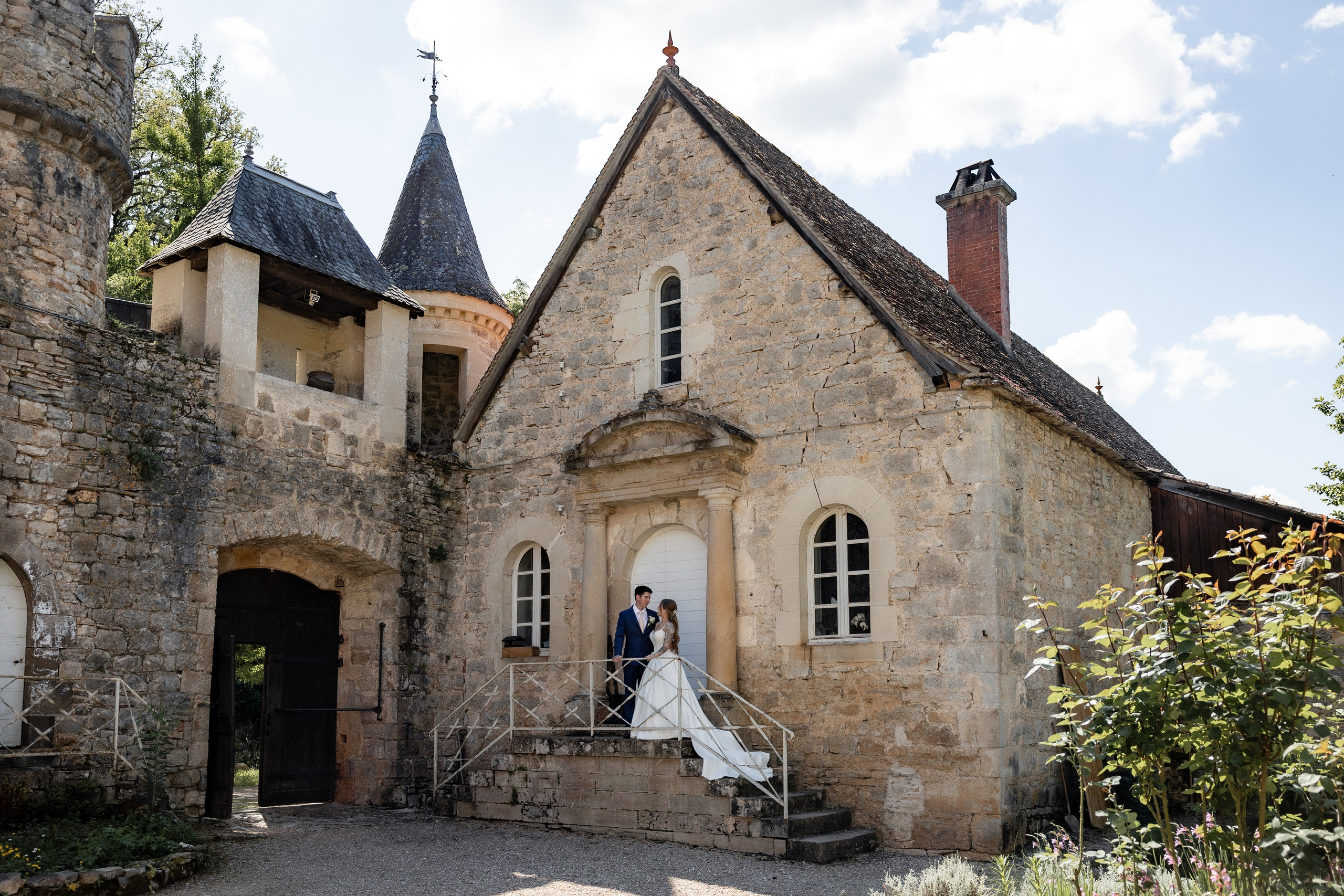 Les mariés s'enlacent devant un château en pierre dans leSud-Ouest de la France lors d'un mariage de destination.Photographie de mariage documentaire par Eugénie Smirnova.