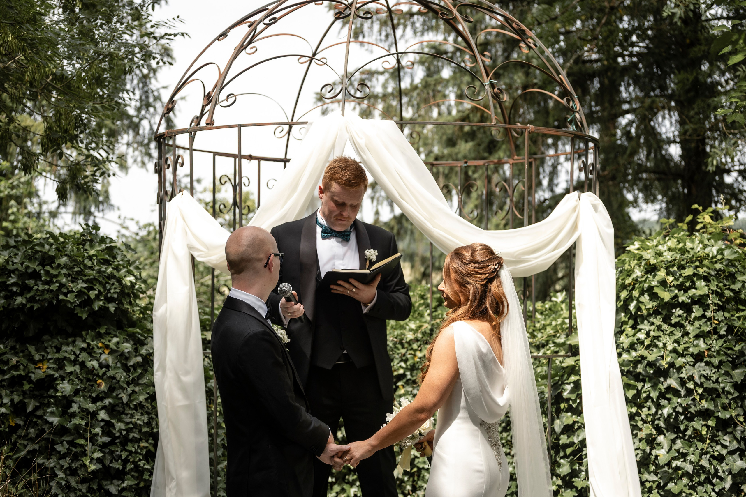 Bride and groom holding hands under a draped iron arbour during the ceremony
