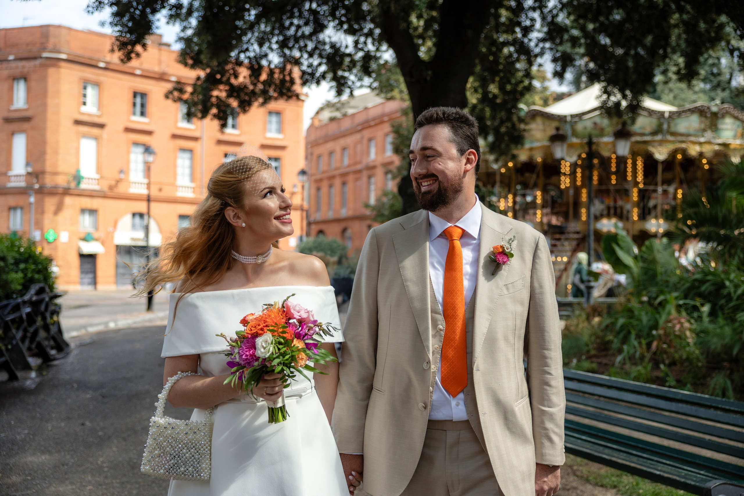 Bride and groom walking past pale facades and greenery at Place Wilson in Toulouse