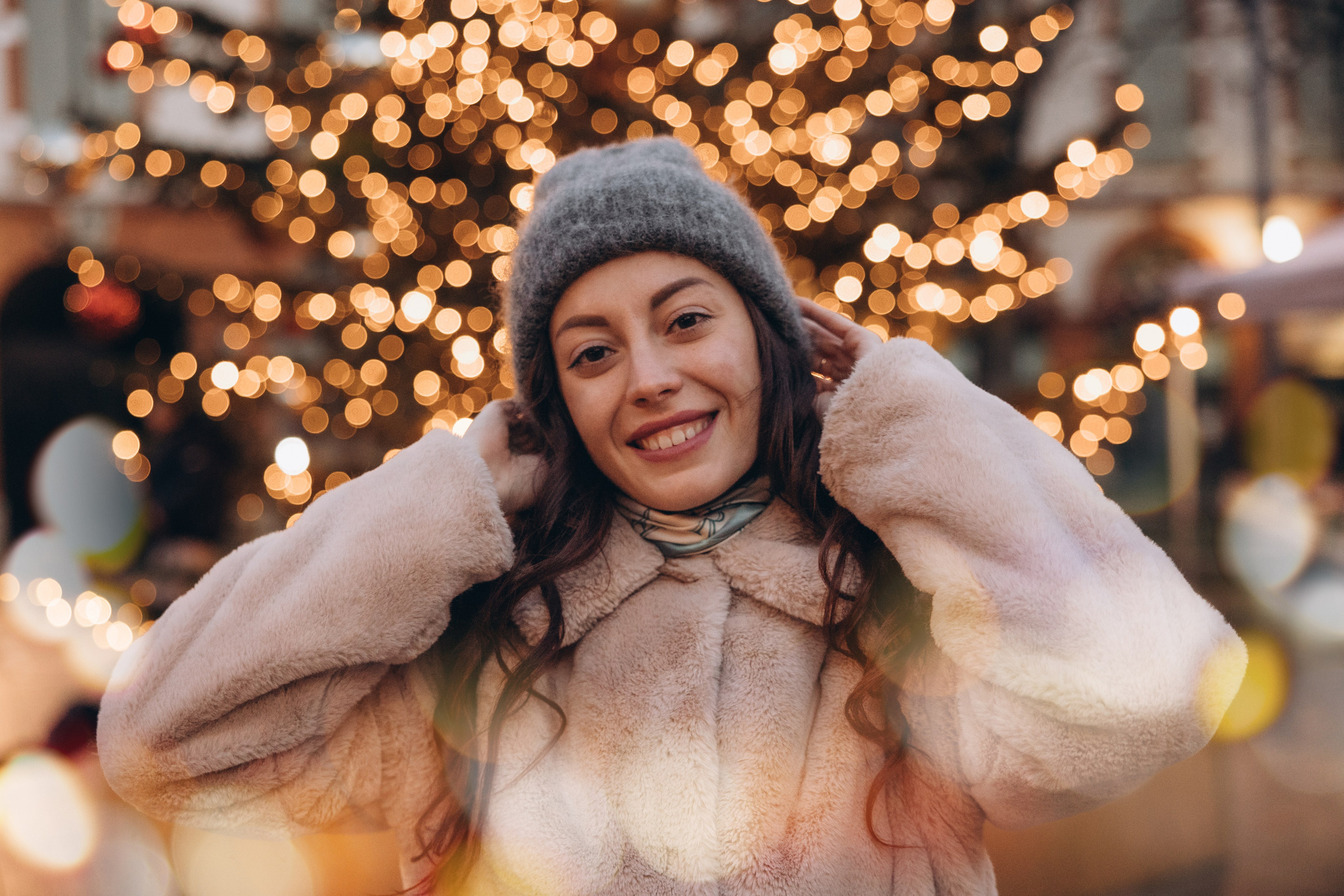 Femme souriante lors d’une séance photo de Noël en extérieur à Toulouse, avec des lumières festives en arrière-plan.