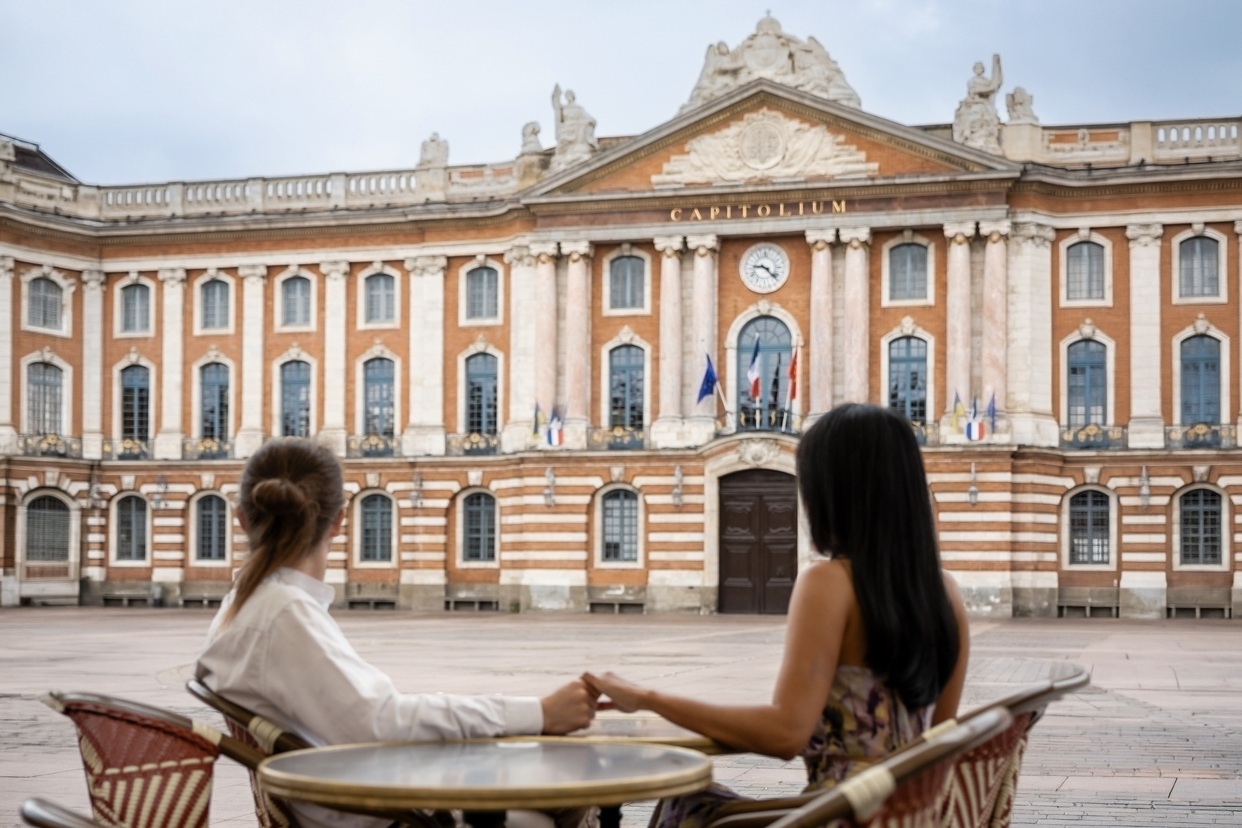 Two people at a café terrace on Place du Capitole in Toulouse, the ornate pink facade behind them