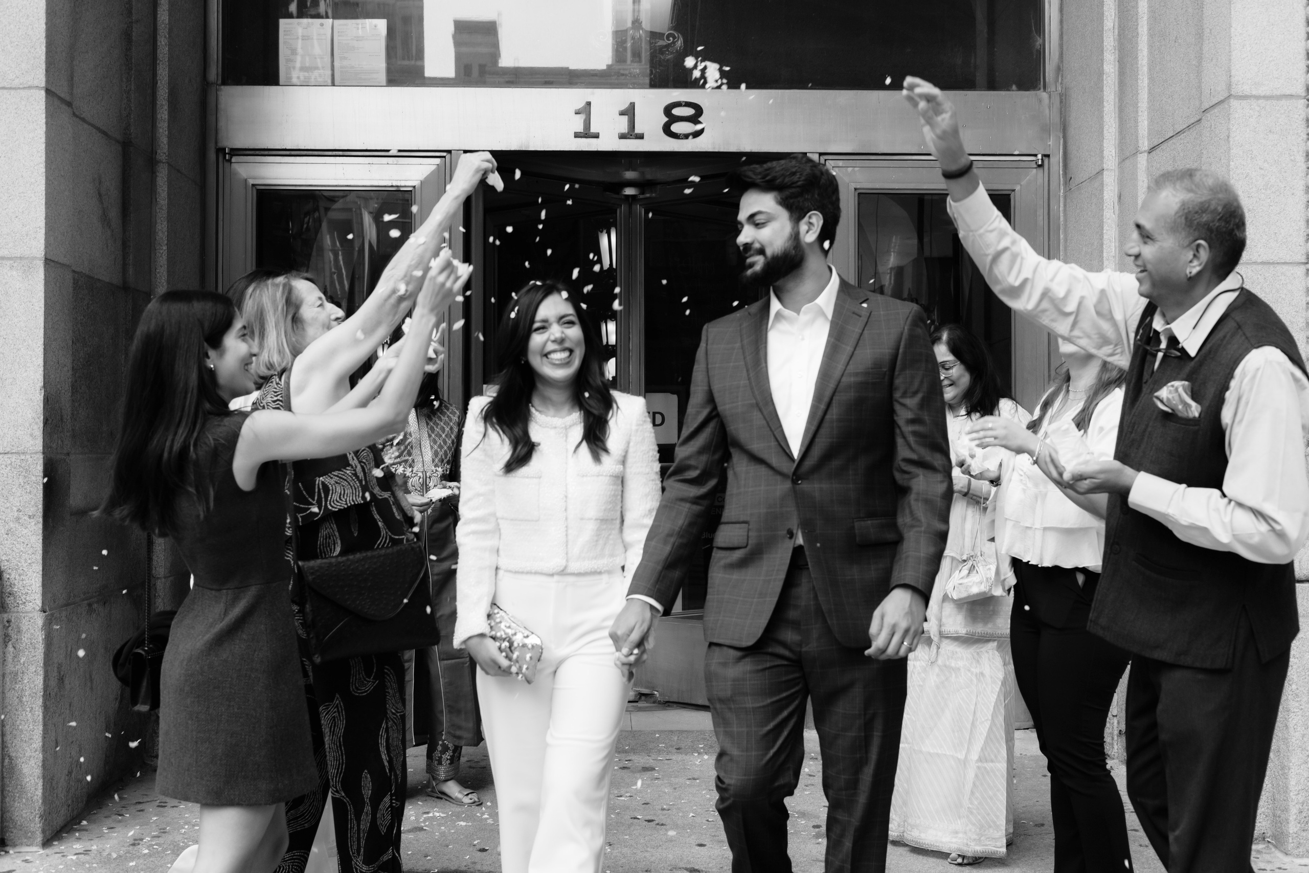 Couple exiting Chicago City Hall while guests throw flower petals and celebrate their courthouse wedding.