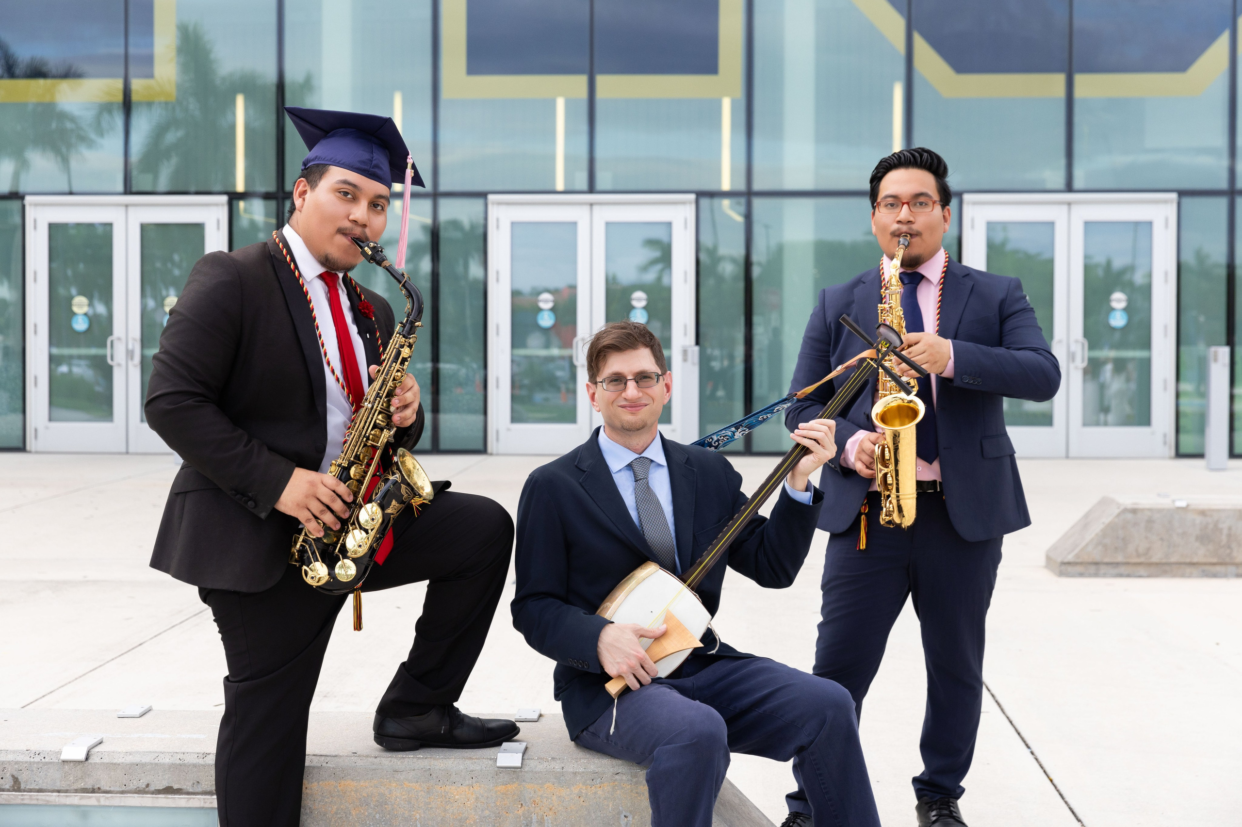 Three FIU music graduates pose together with saxophones and a clarinet.