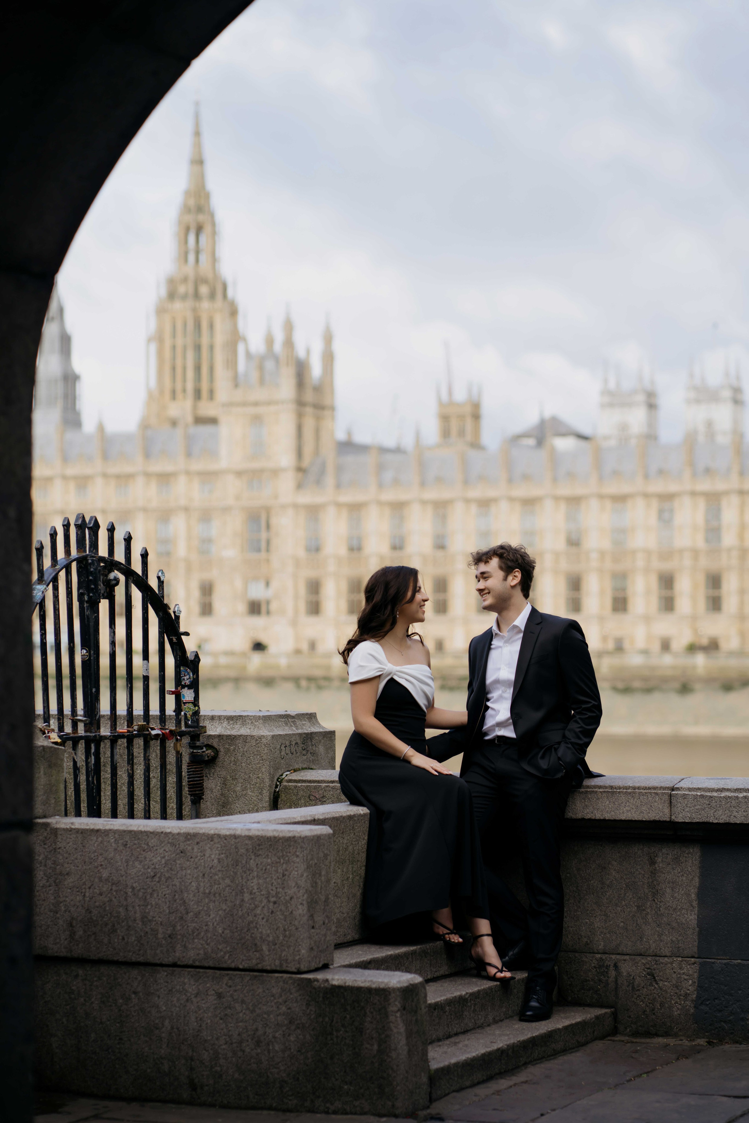 Couple embracing during London engagement photoshoot with Westminster architecture in background.
